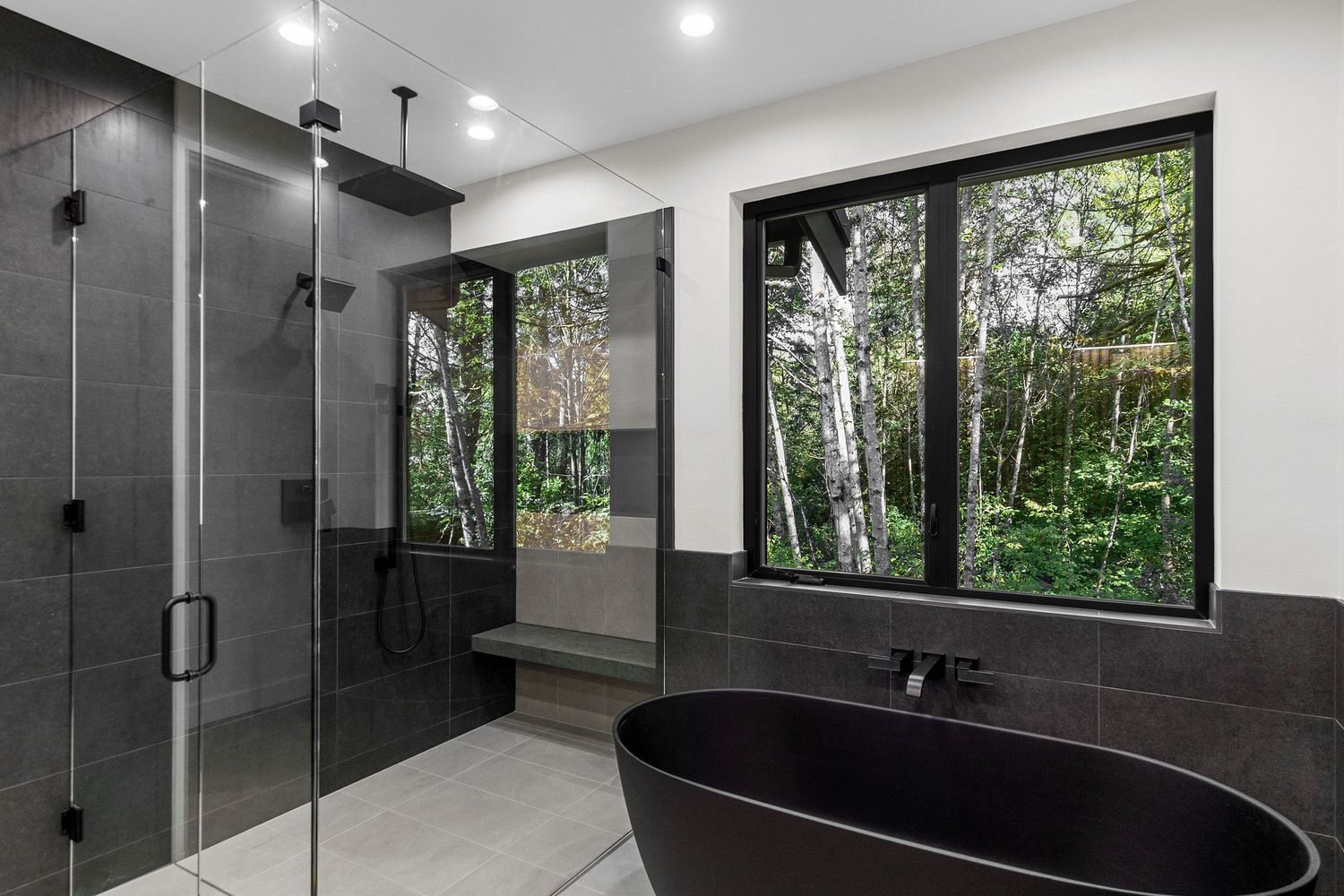 Contemporary bathroom with black tile walls, glass shower enclosure and large windows bringing in natural light.