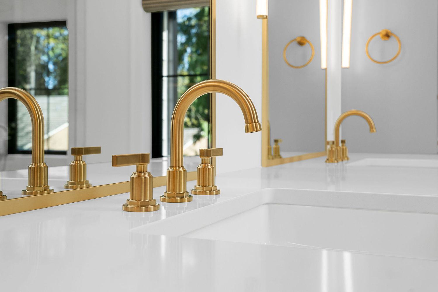 Row of gold faucets on white countertop with brass fixtures and mirror reflections.