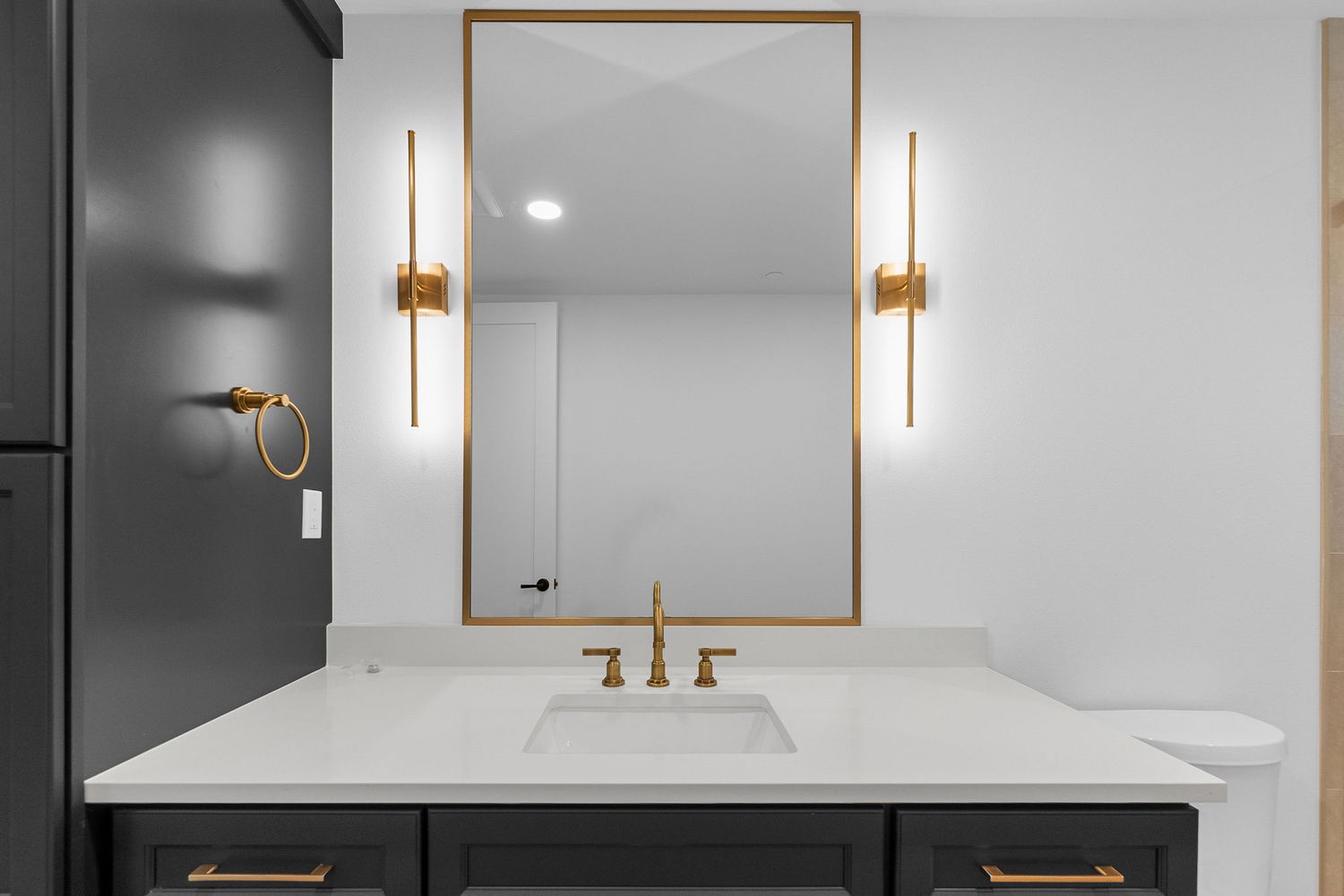 Modern bathroom vanity with gold fixtures, framed mirror, and wall sconces.