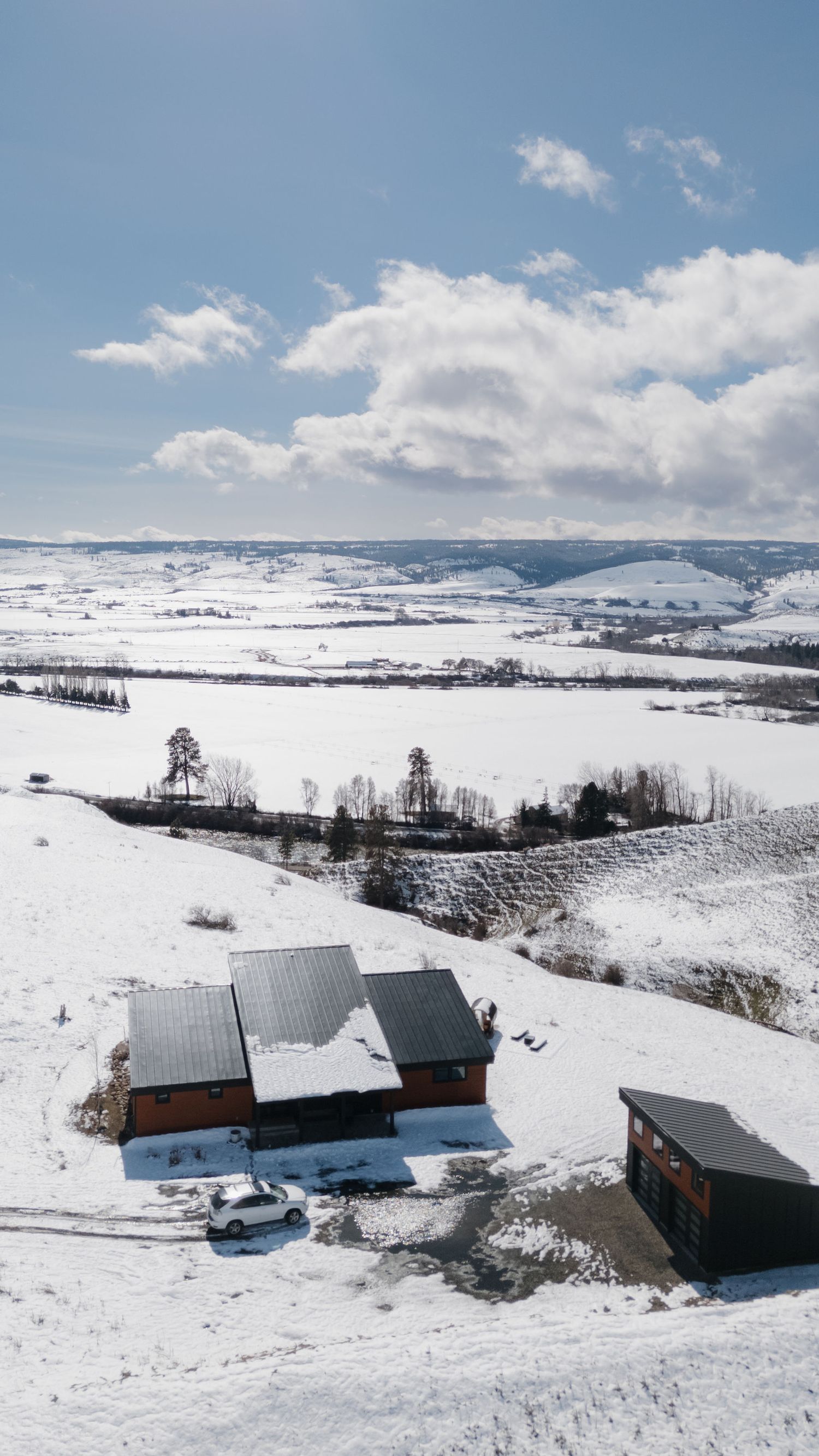 A panoramic winter landscape shows snow-covered houses and barns nestled in rolling white hills under a bright blue sky.