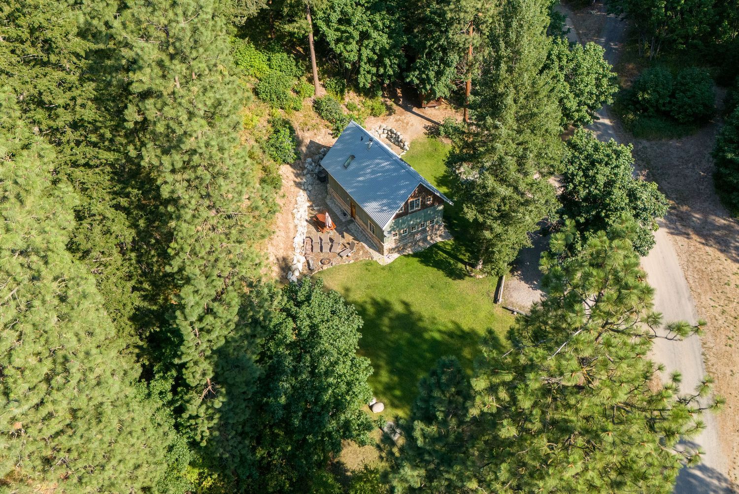 Drone perspective of log cabin property with trees and natural landscaping features.