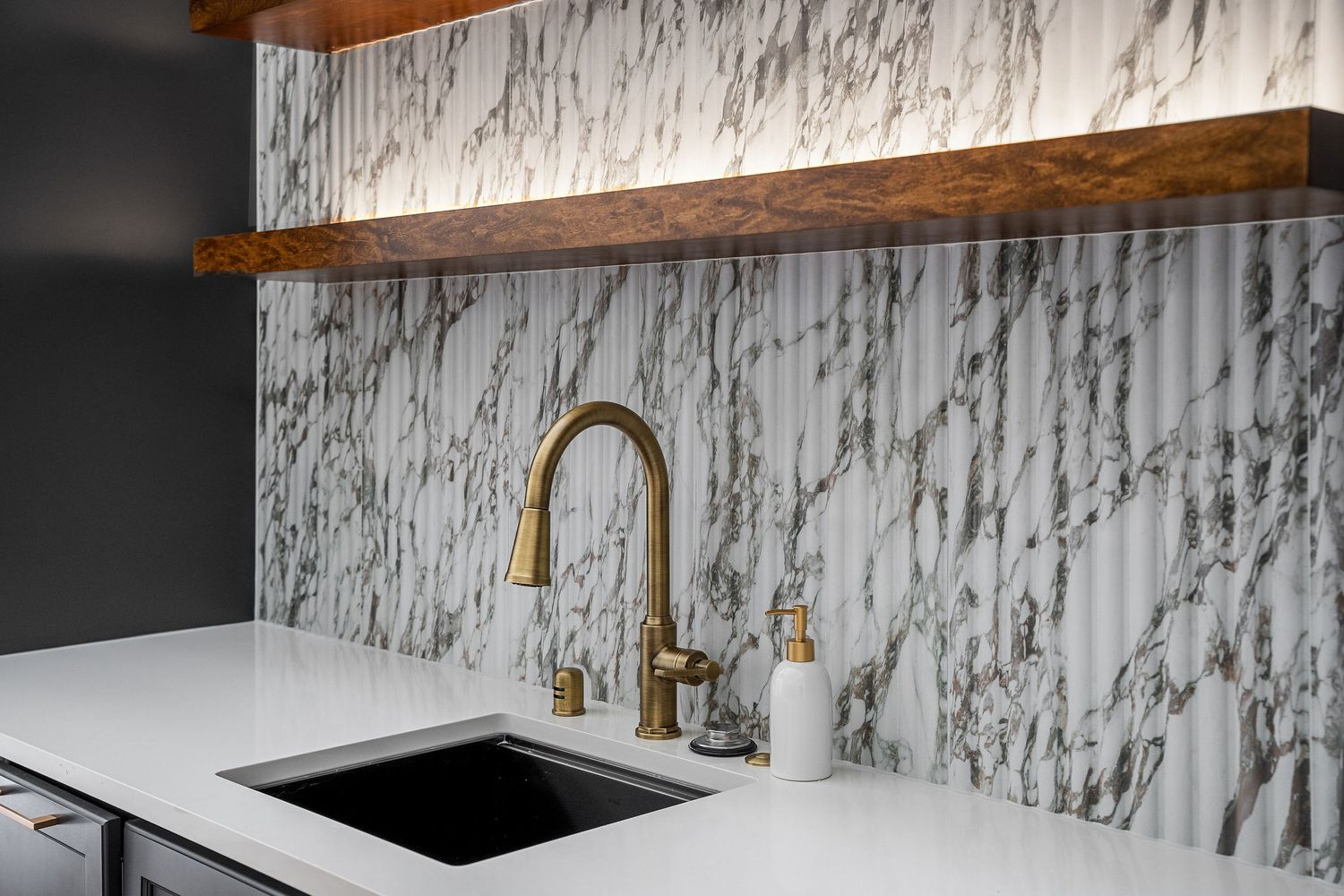 Modern kitchen interior with white marble backsplash, brass fixtures, and wood accents creates an elegant design aesthetic.