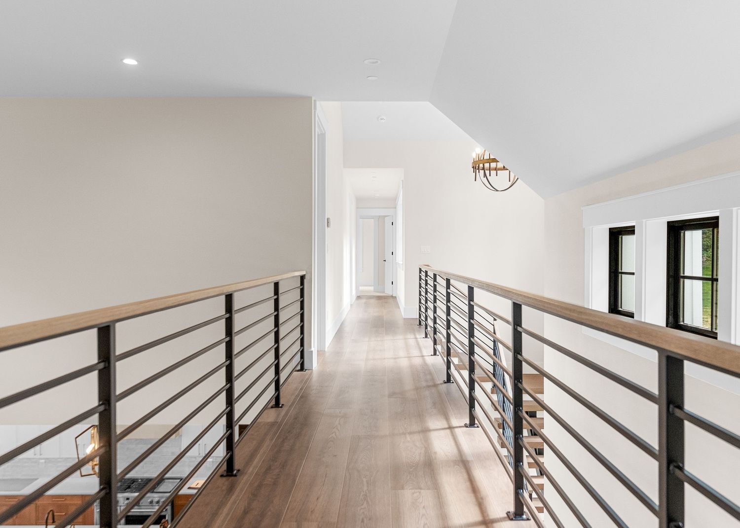 Modern hallway with black metal railings and hardwood flooring leading to bright windows.