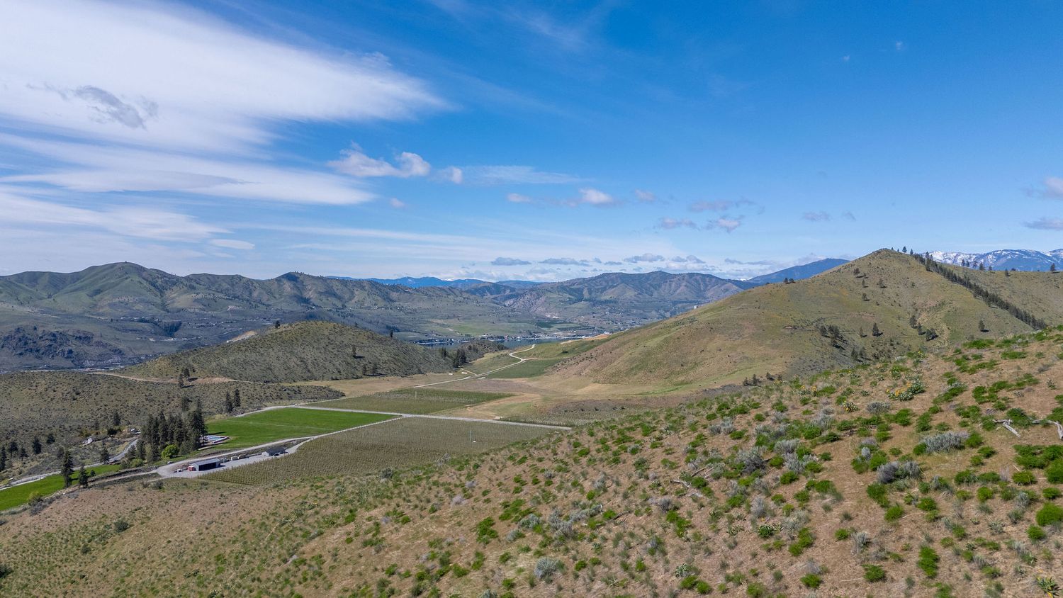 Panoramic view of rolling green hills and distant mountain ranges under a blue sky in a scenic rural landscape.