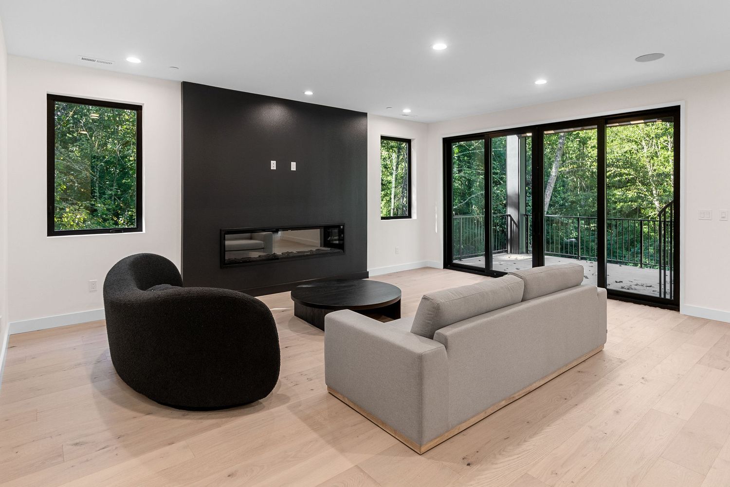 Spacious open concept living area with white walls, recessed lighting and large windows overlooking nature.
