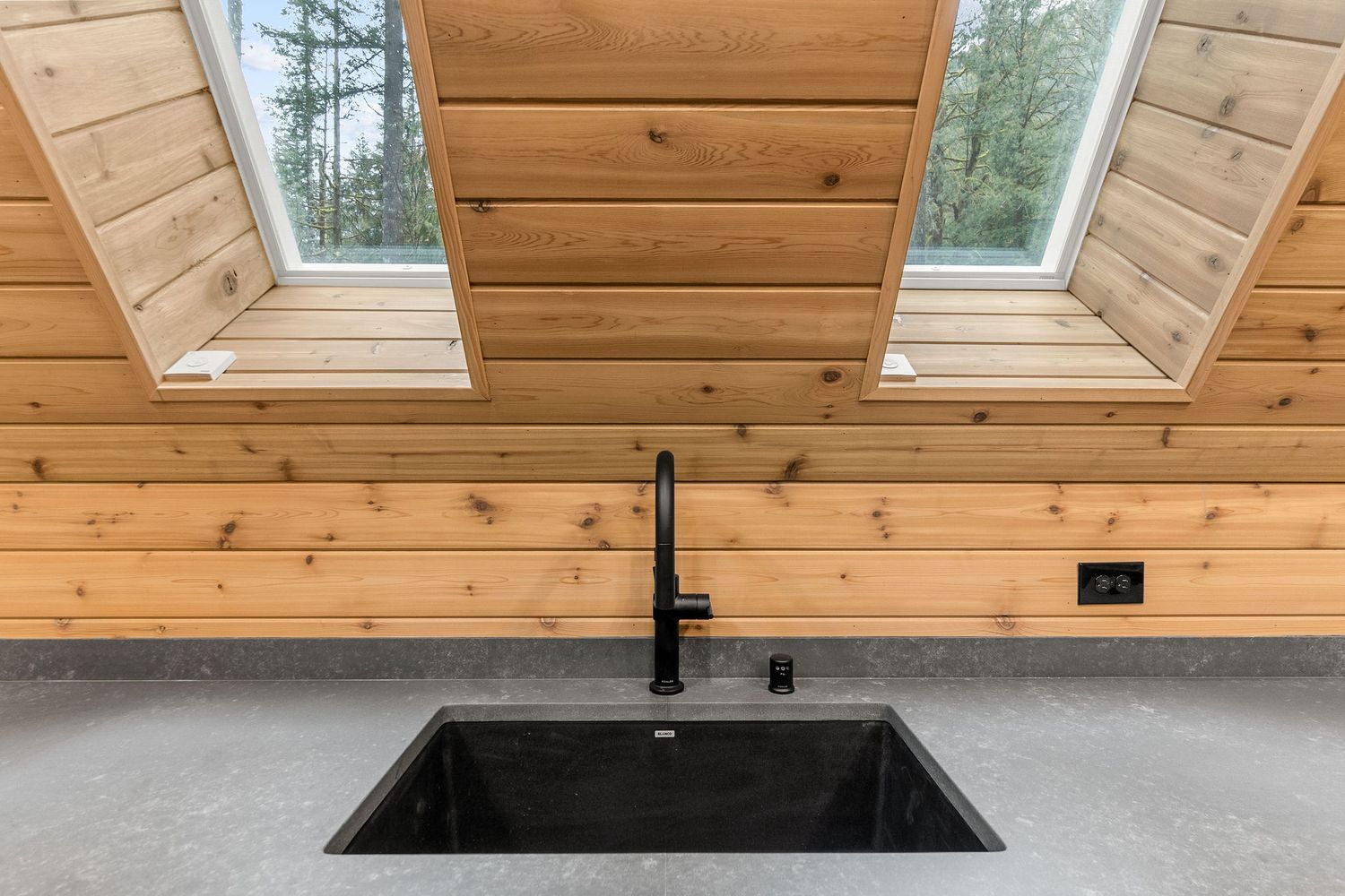 Modern black sink and faucet with grey countertop under skylights in wooden interior.