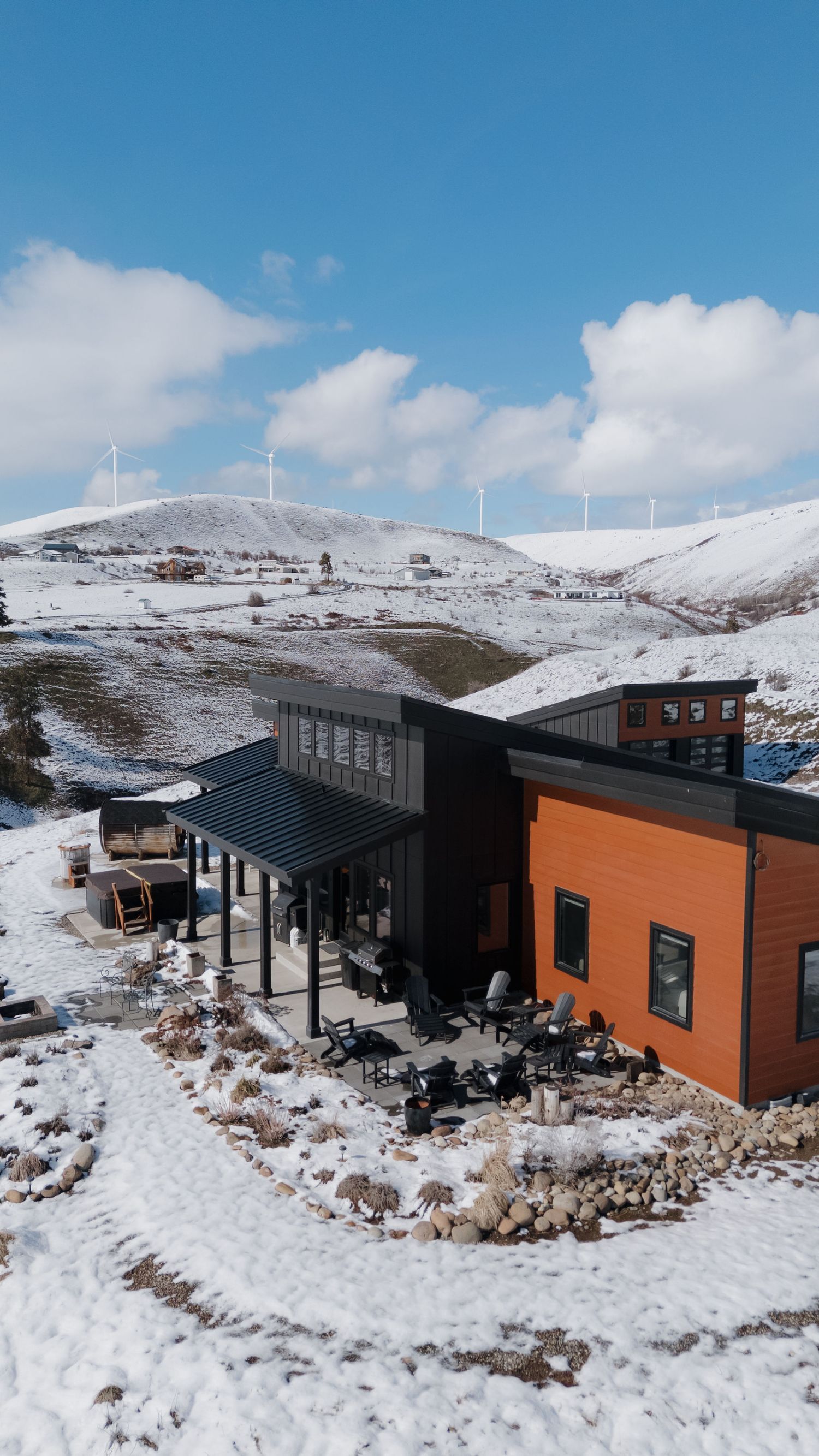 Modern cabin lodges with black and orange exterior nestled in snowy mountain landscape on sunny winter day.