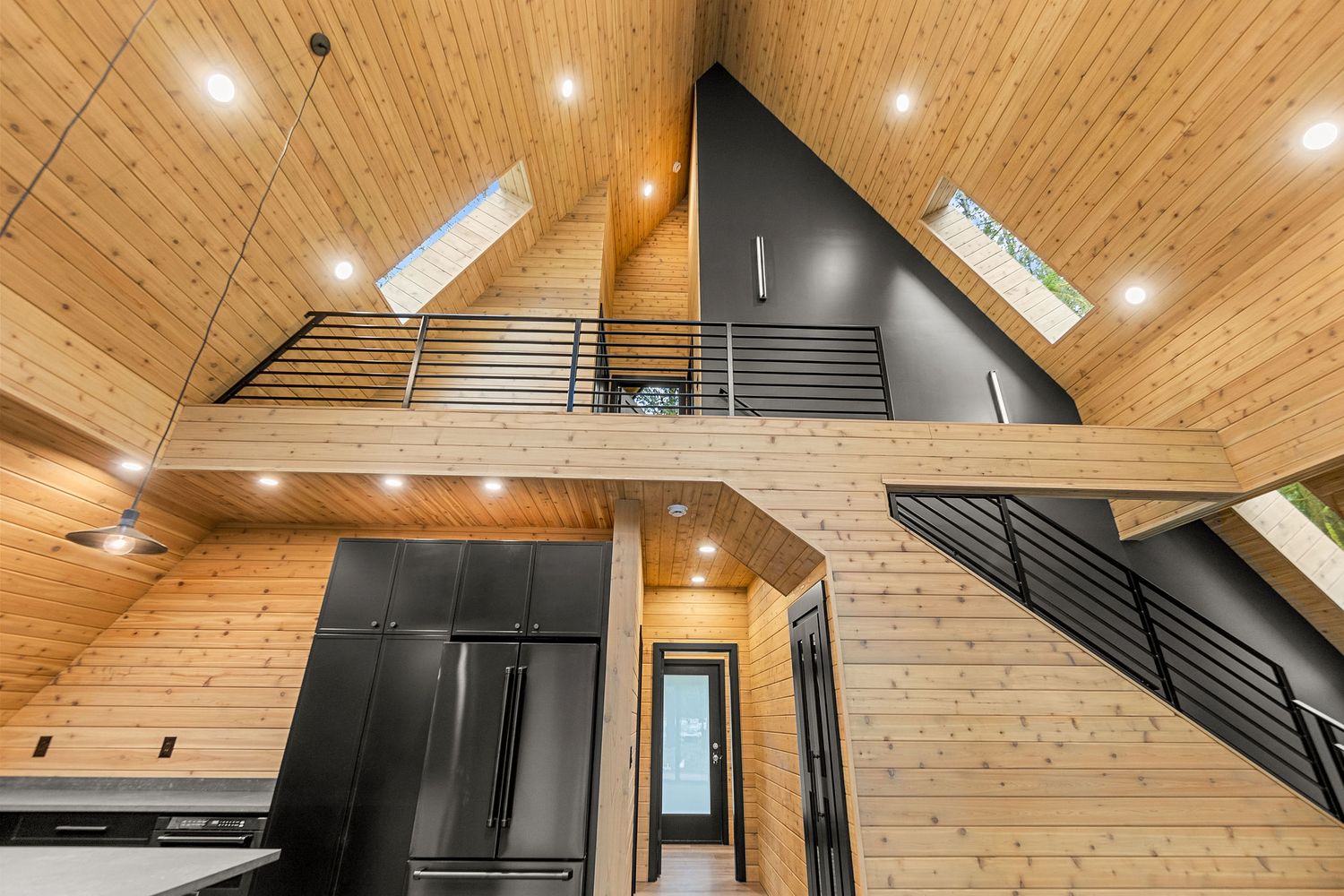 High ceiling A-frame interior with black stairs, modern kitchen, and natural wood finishes.