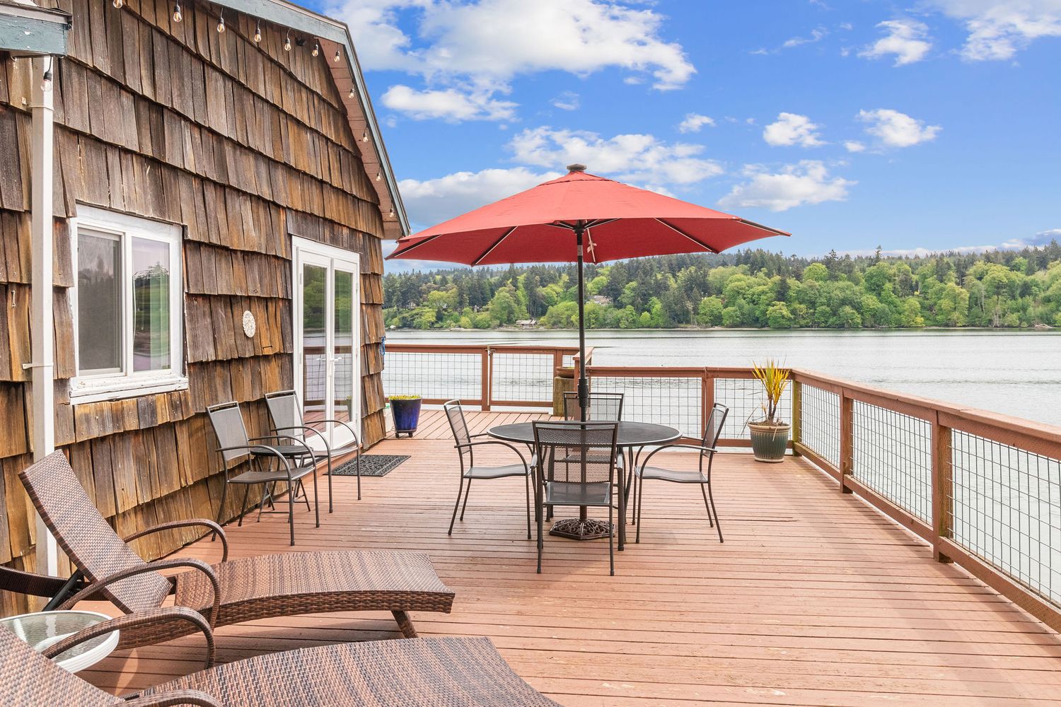 Expansive wooden deck with red patio umbrella and lounge furniture overlooking scenic waterfront views.