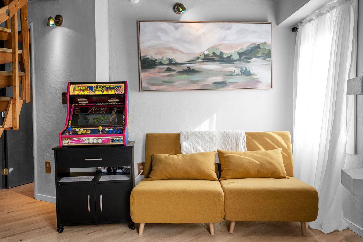 Modern living room with mustard yellow sofa, arcade machine, and white walls.