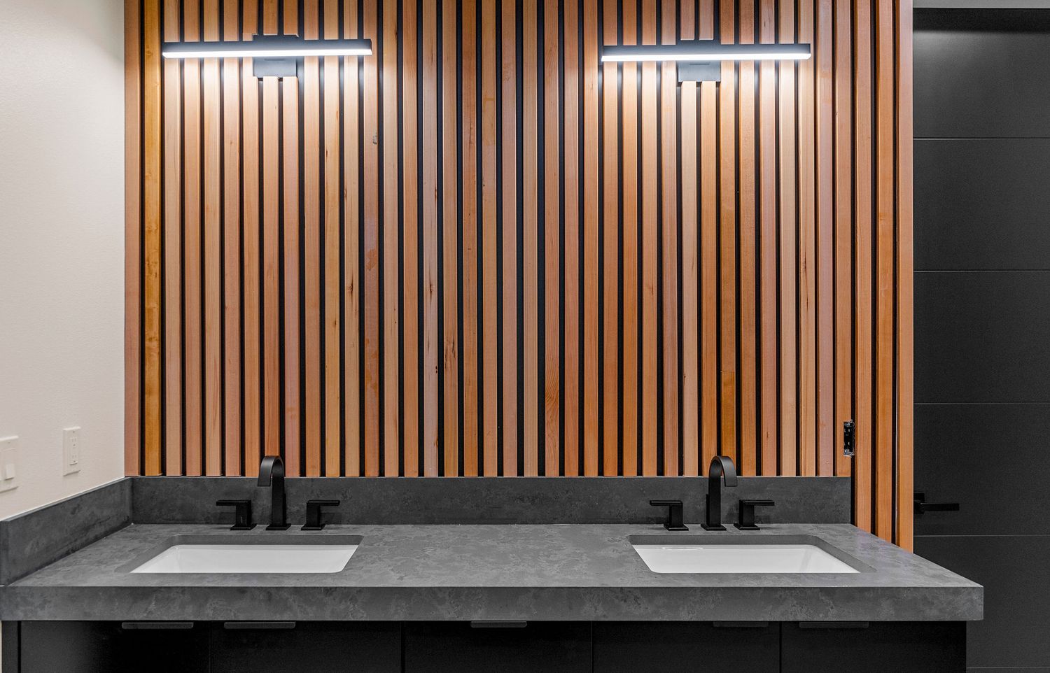 Contemporary wooden slat wall accent with dual black sinks and modern fixtures in elegant bathroom setting.