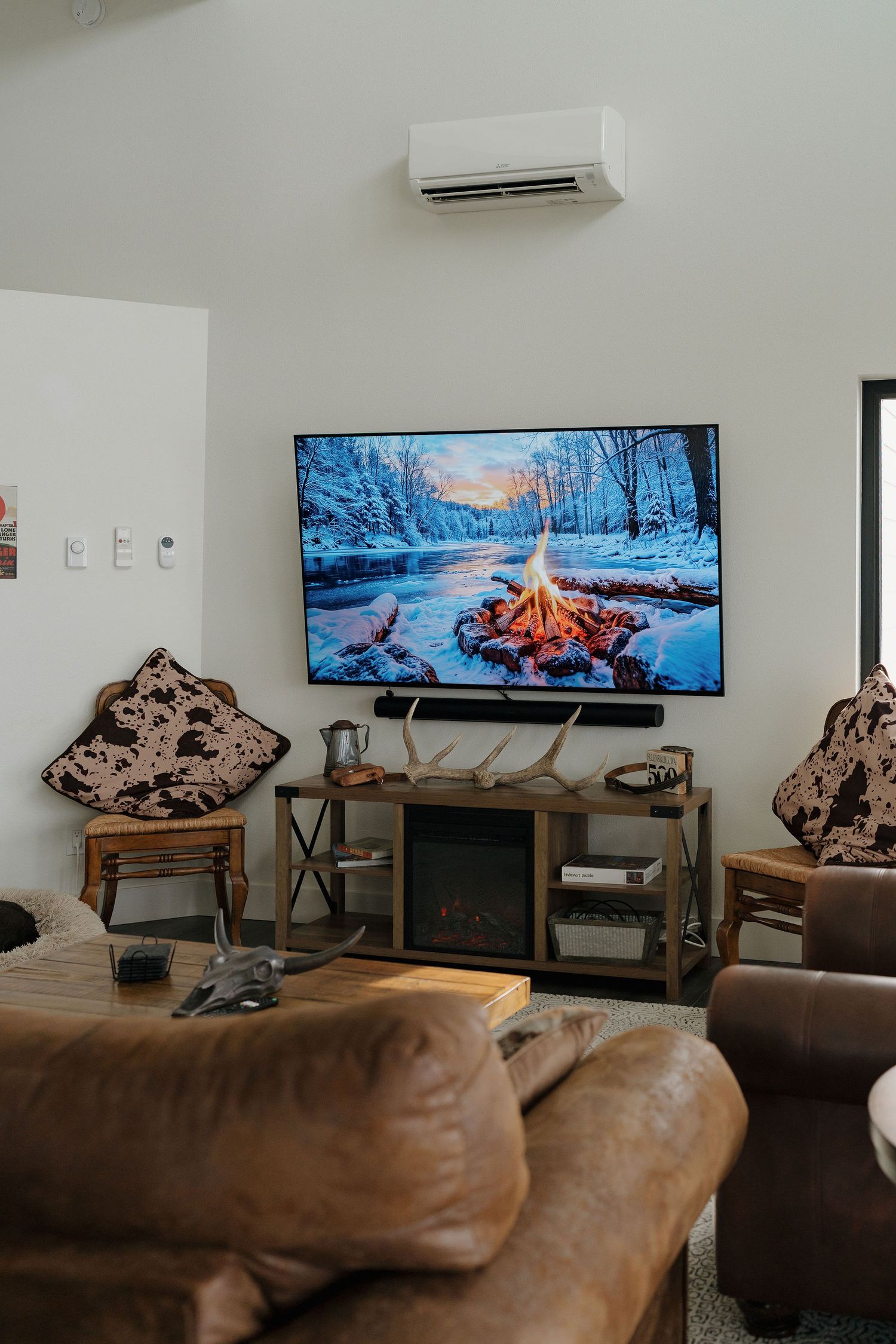 Modern living room interior with wall-mounted TV displaying winter scene and brown leather furniture.