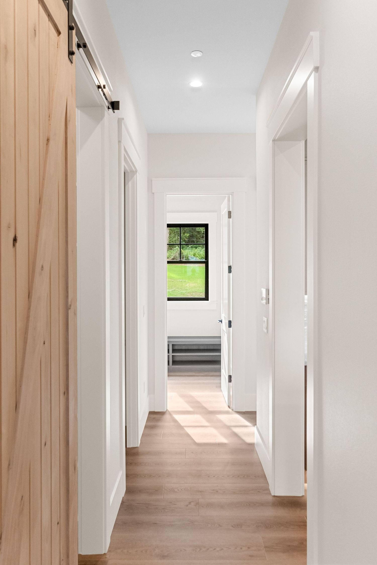 Long hallway with white walls, light wood accents, and natural light streaming through windows.