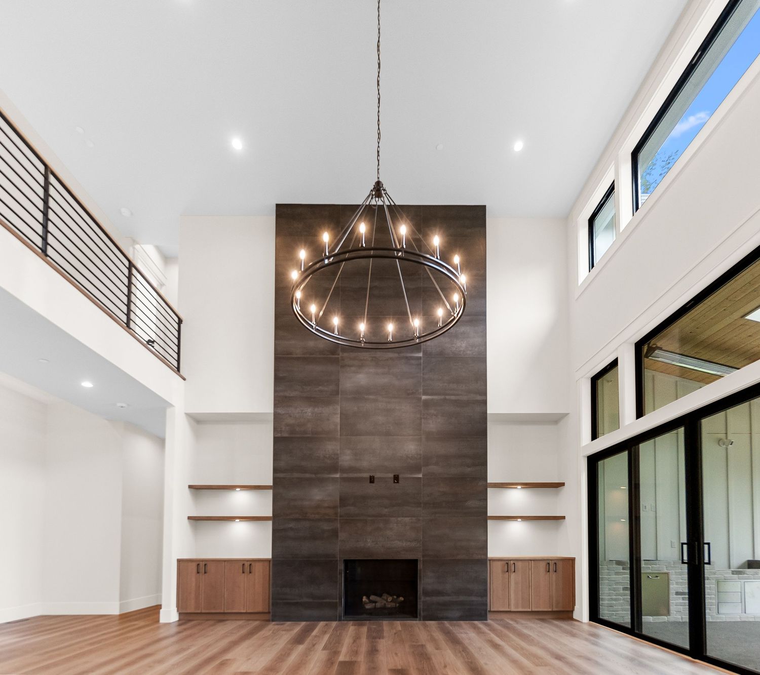 Grand living room with two-story ceiling, wood accent wall, and large circular chandelier.