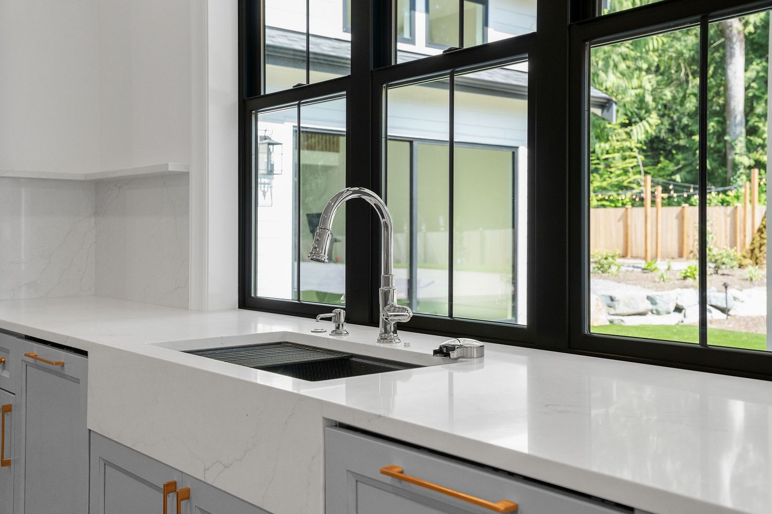Modern farmhouse sink with black-framed windows and brass hardware in white kitchen.