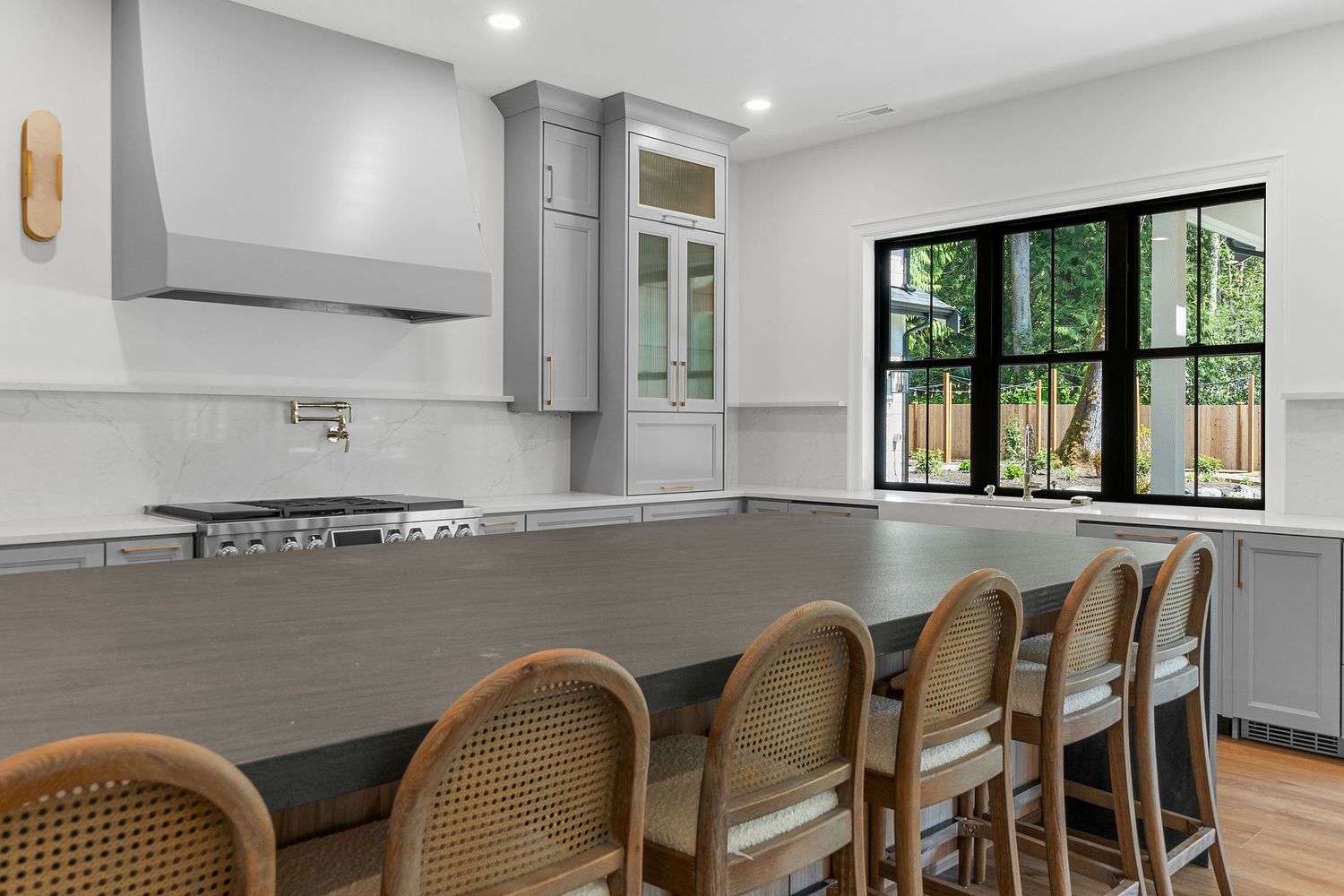 Contemporary kitchen with gray cabinets, pot filler, and rattan counter stools along island.