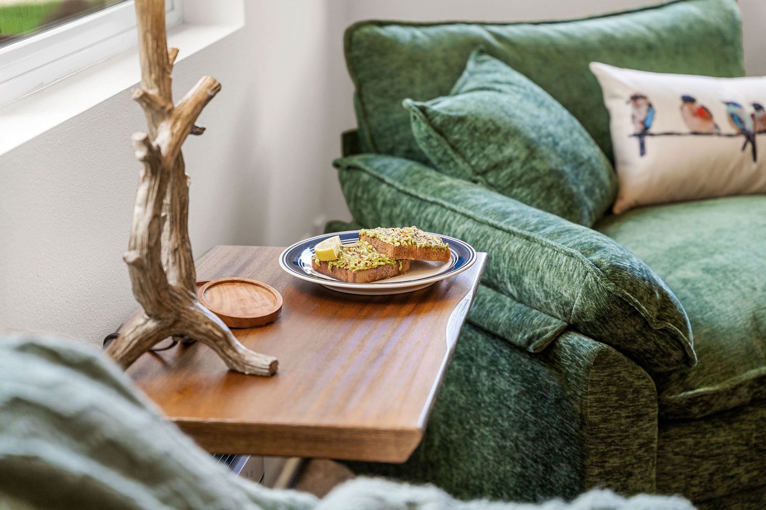 Close-up of plush green velvet sofa with decorative pillows and wooden side table.