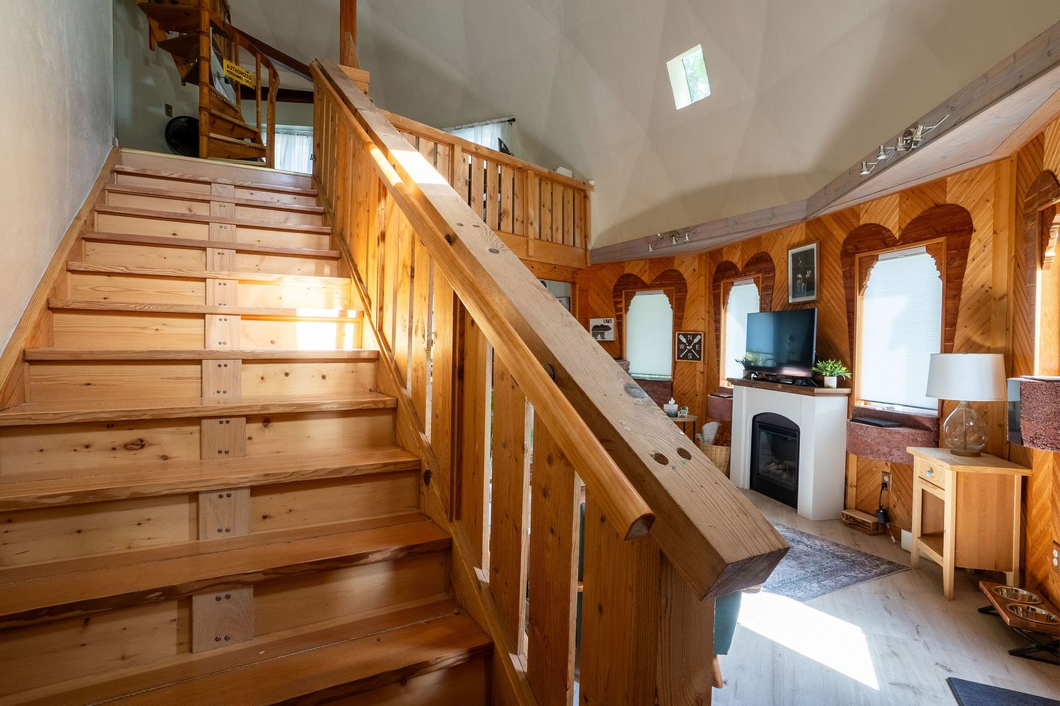 Light-filled stairwell with natural wood railings and white walls in a modern cabin.