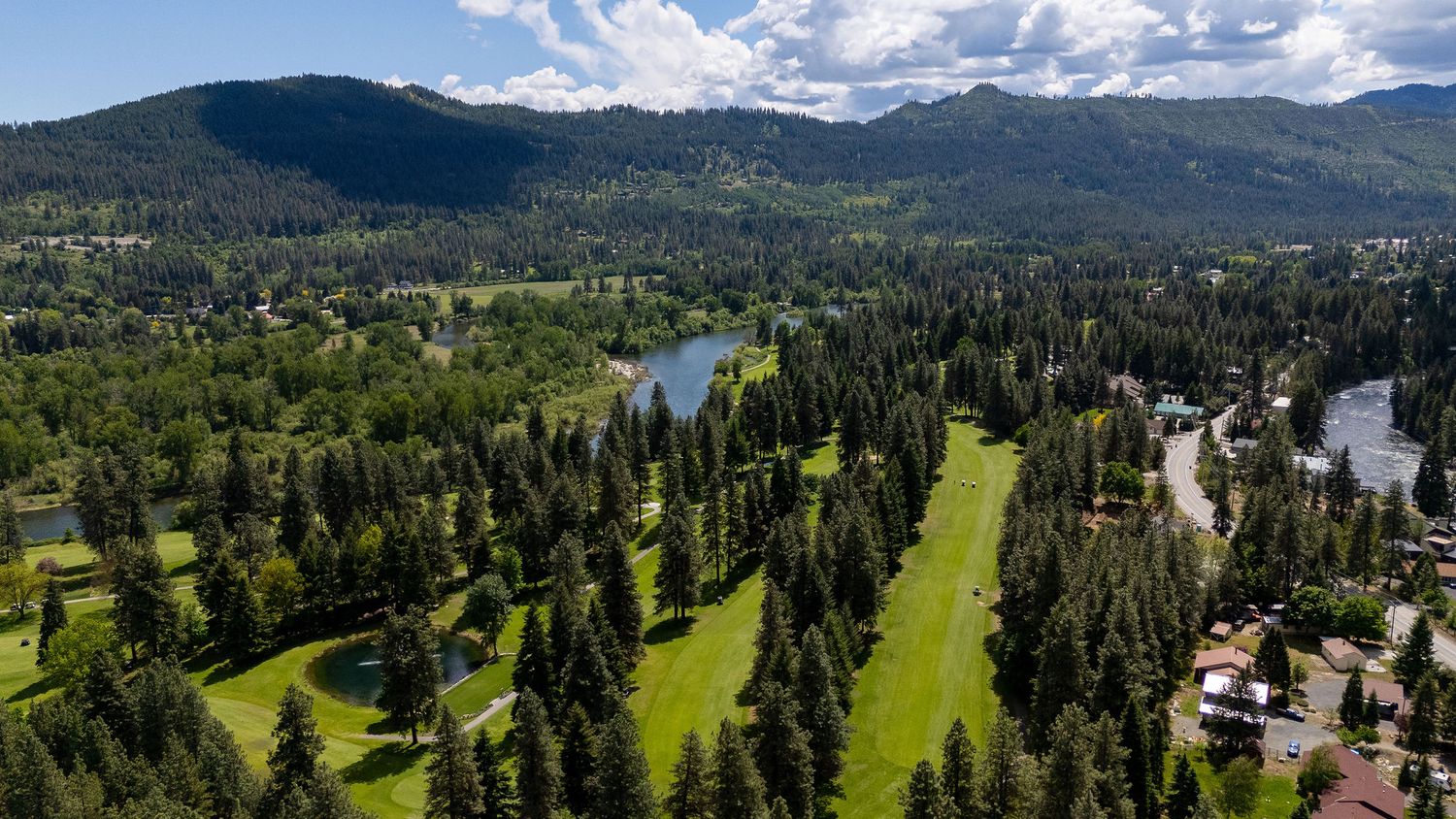 Aerial view of mountain valley with golf course and residential development surrounded by forest.