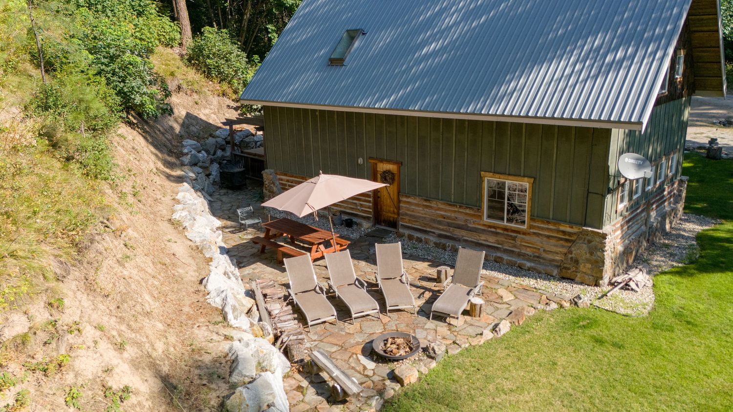 Modern cabin with metal roof and outdoor patio area surrounded by natural landscaping.