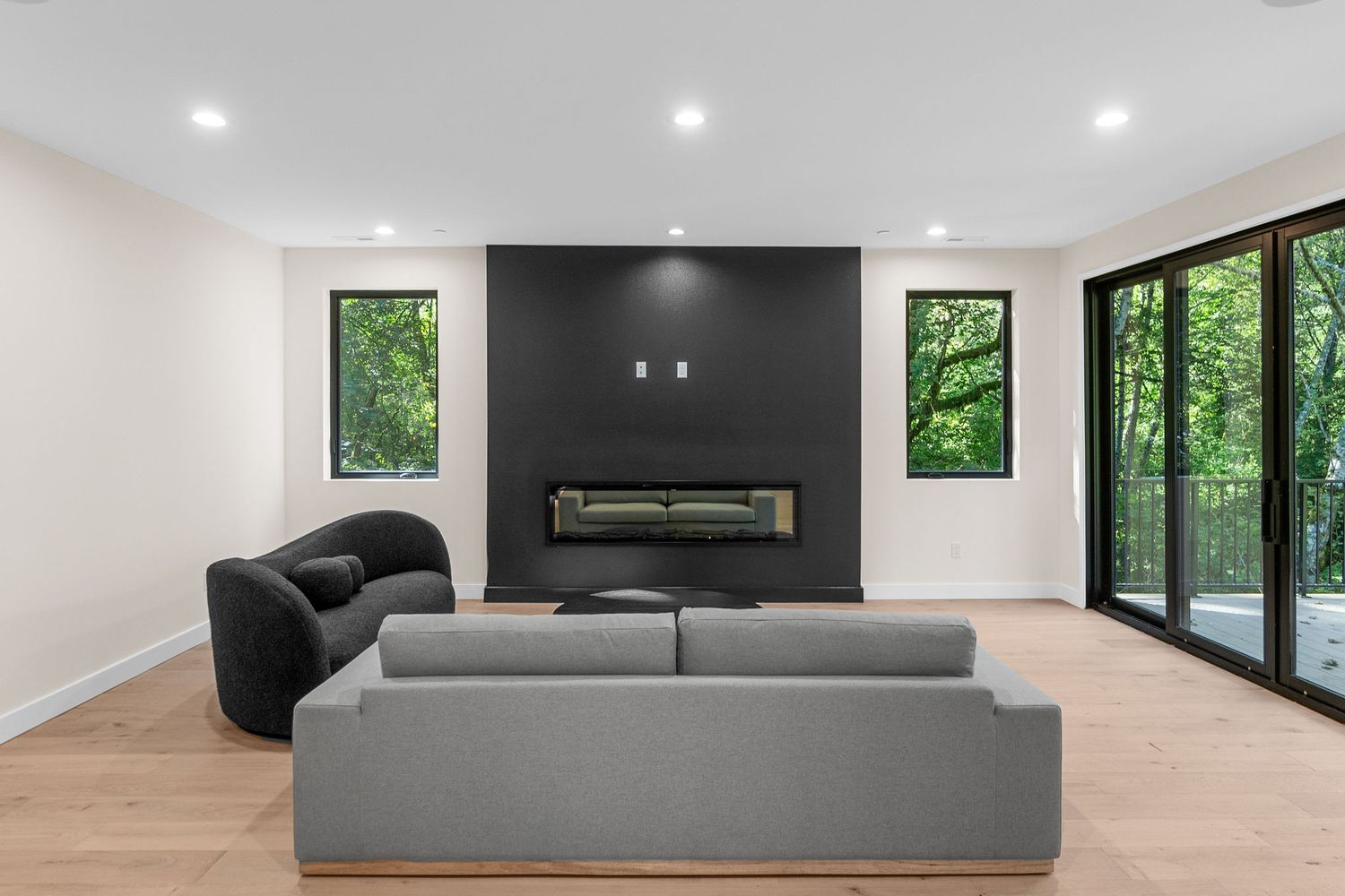 Contemporary living room with grey sofa, black fireplace, and floor-to-ceiling windows.