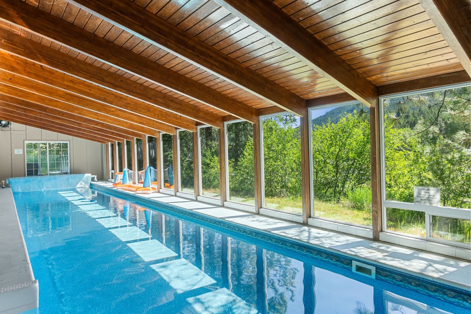 Indoor swimming pool with wood-paneled ceiling and large windows offering views of surrounding forest scenery.