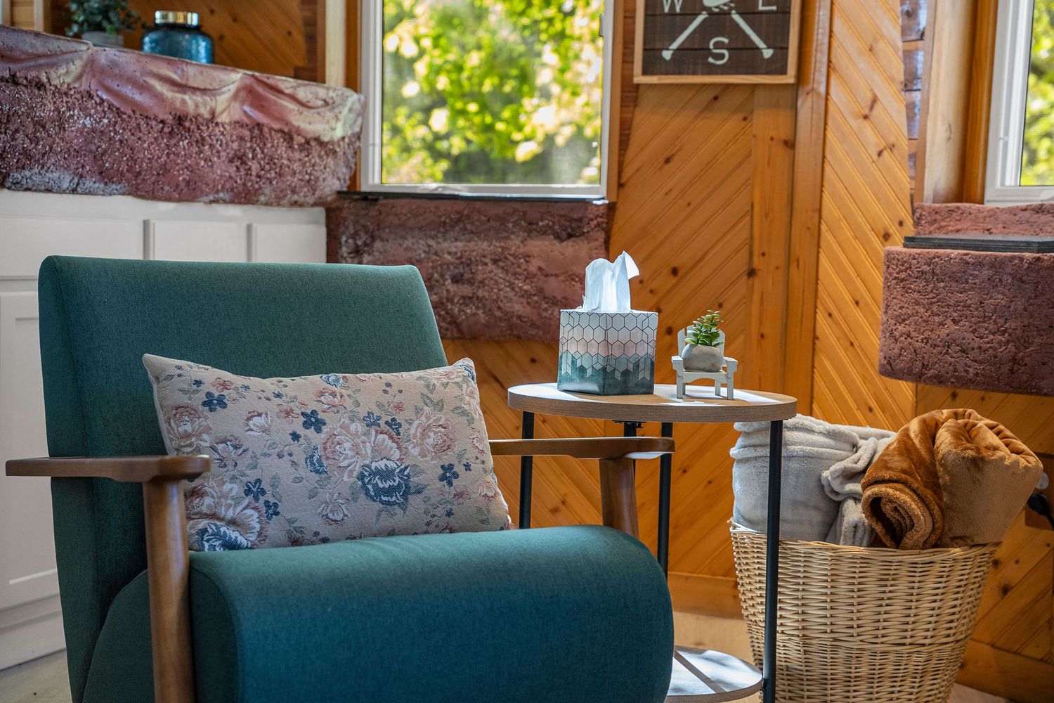 Cozy cabin interior with green armchair, rustic wood walls, and natural sunlight streaming through windows.