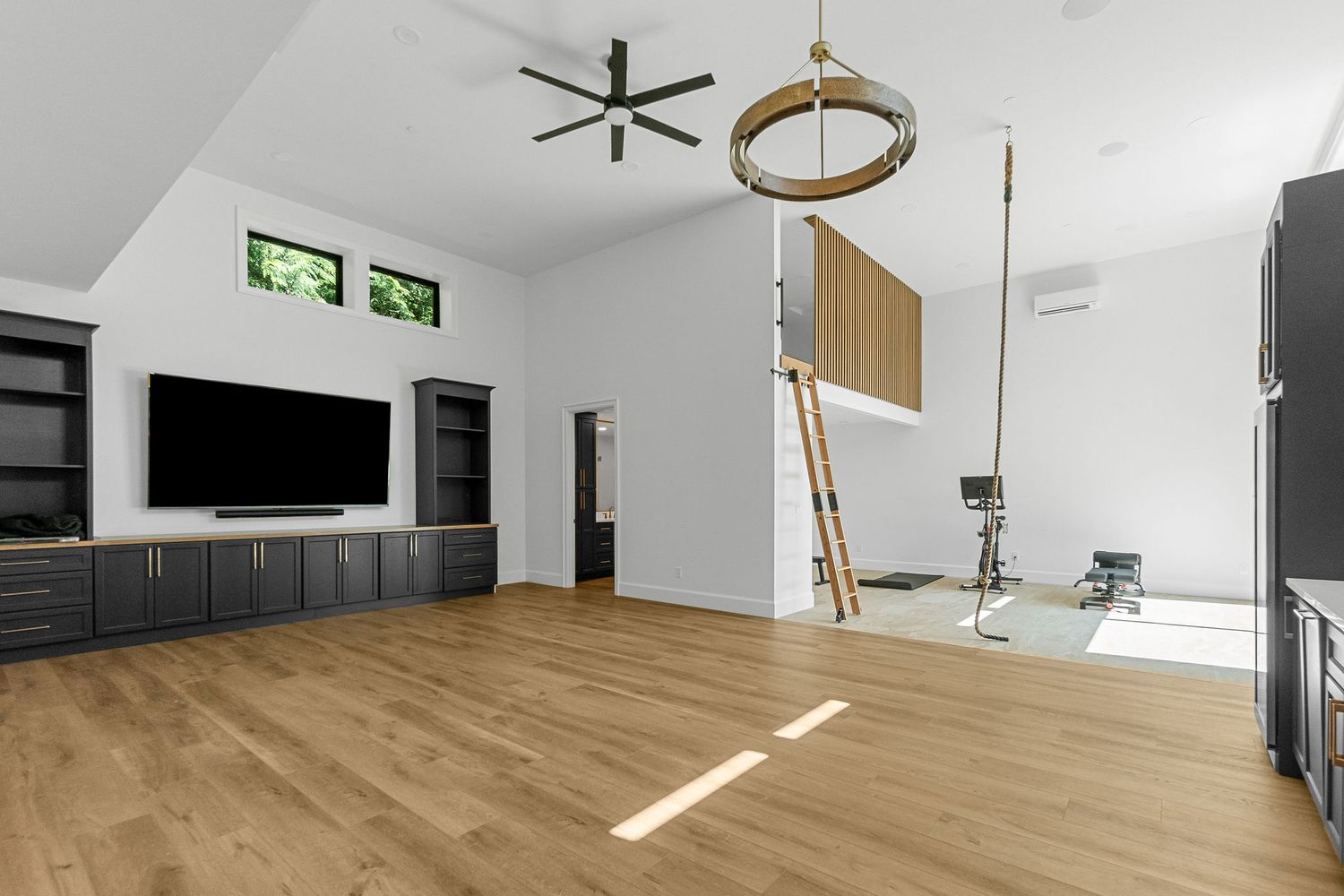Spacious room with hardwood floors, black media cabinet, and vaulted ceiling with fan.