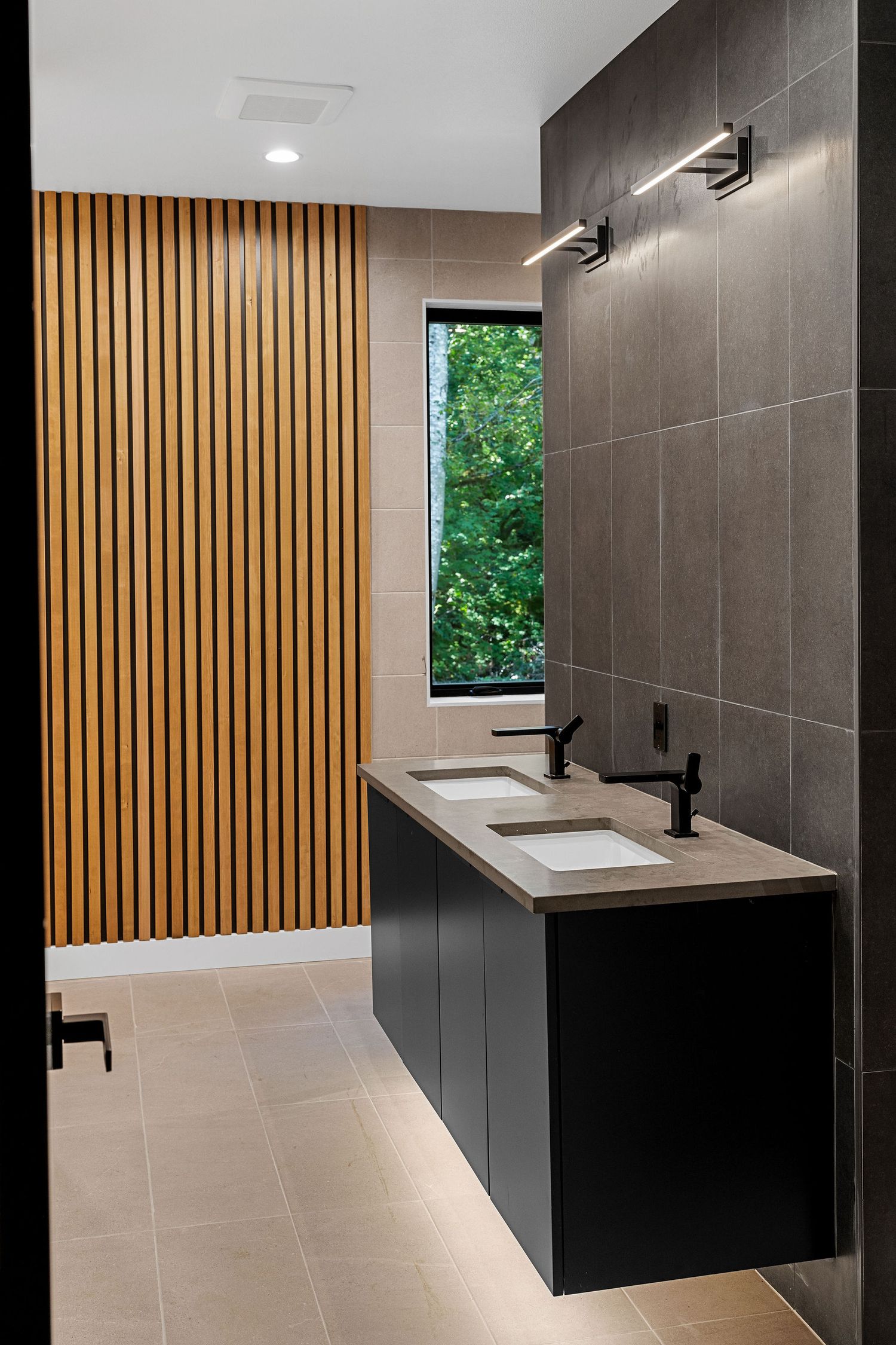 Modern bathroom featuring dark tile walls, wooden slat accent wall, and floating vanity.