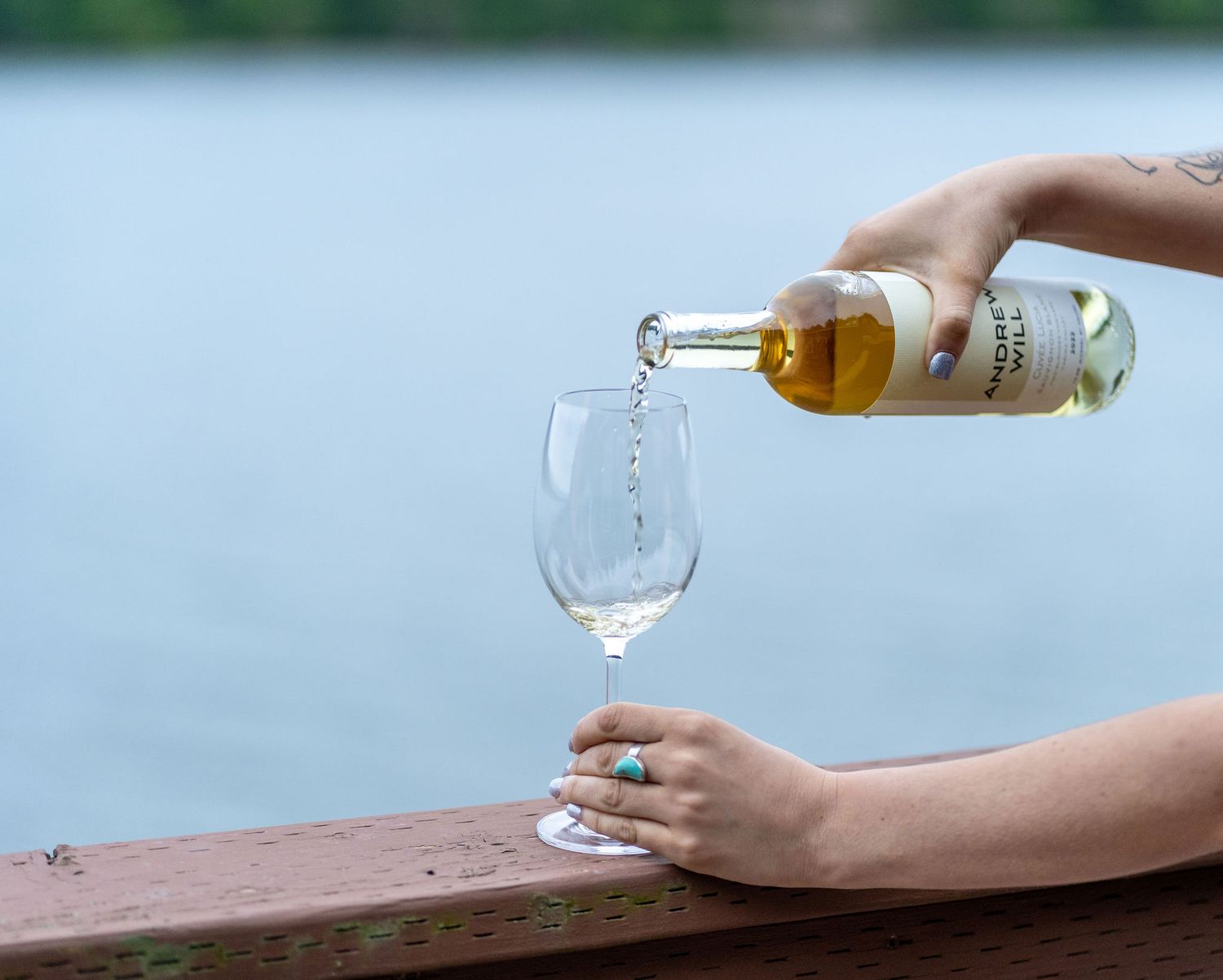 White wine being poured into a glass on outdoor deck railing.