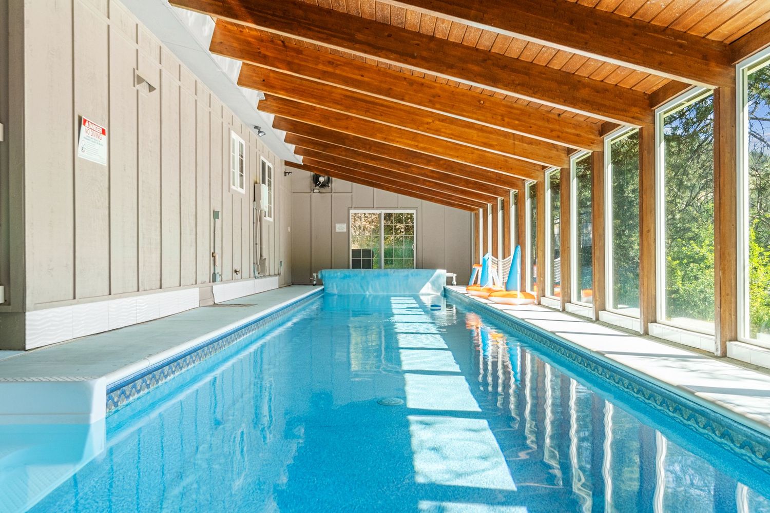 Indoor swimming pool with wood beam ceiling and floor-to-ceiling windows.