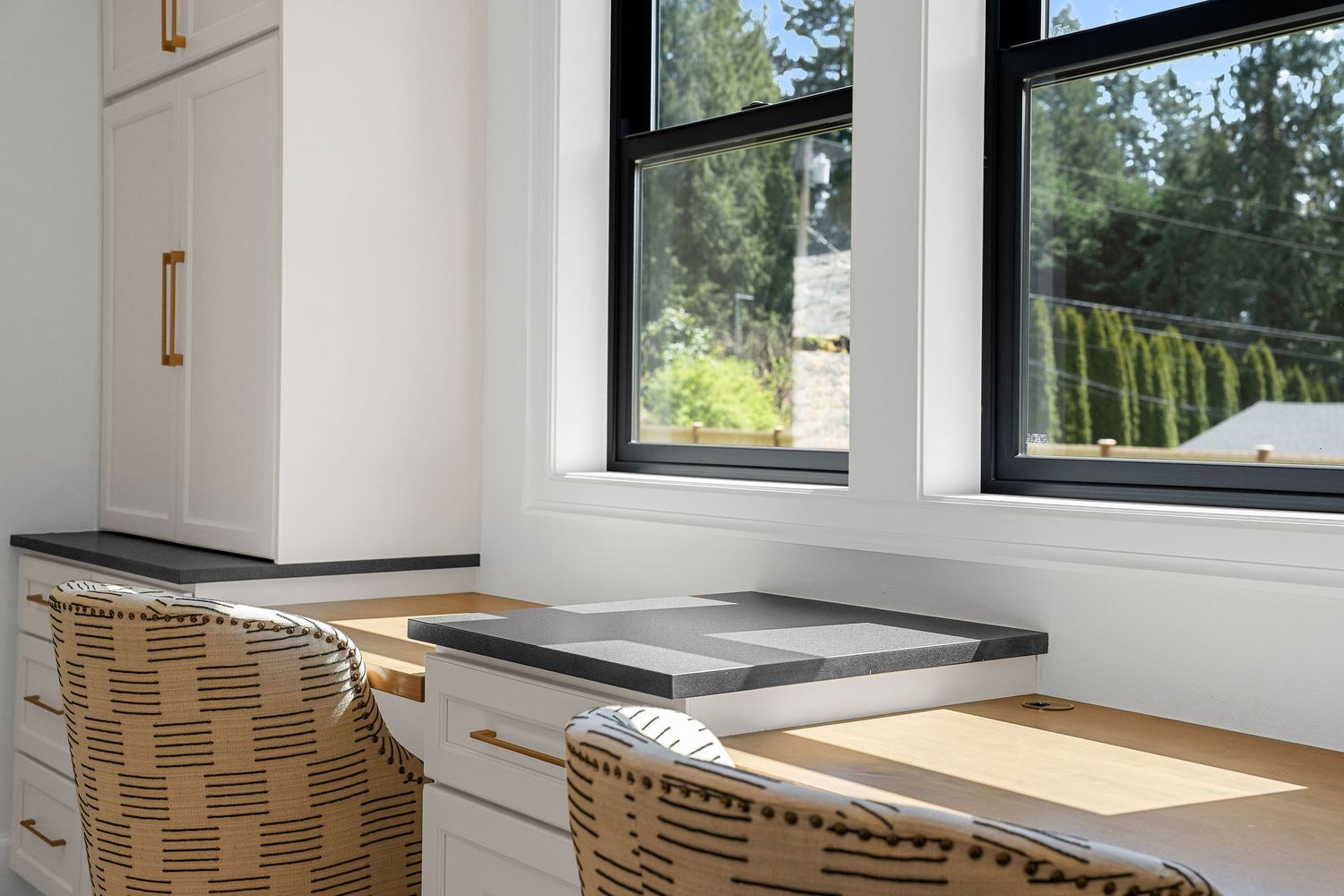 Long built-in desk setup with woven chairs and storage cabinets along a windowed wall.