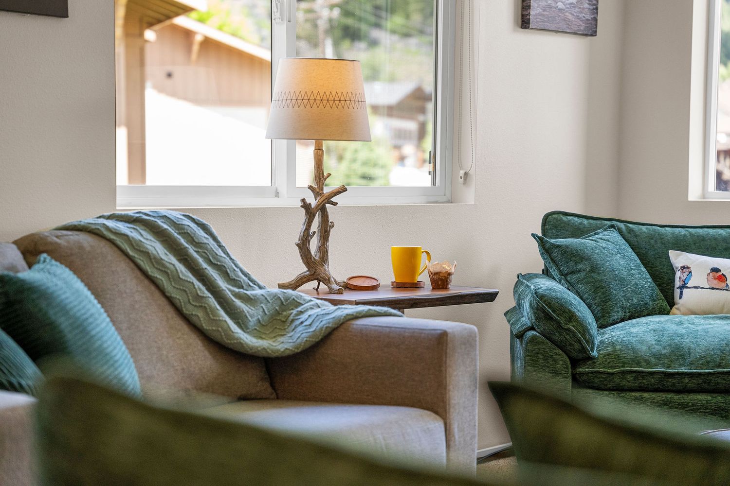 Modern living room with blue-green couch and mountain-themed decor in natural lighting.