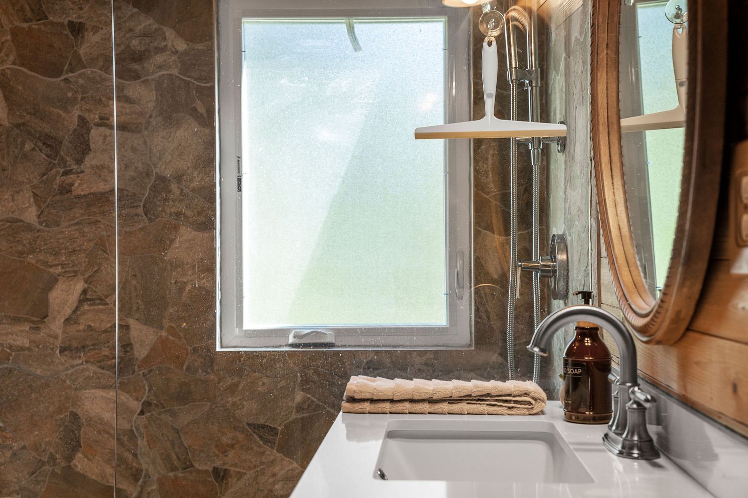 Rustic stone bathroom with natural light streaming through window and circular mirror on wall.
