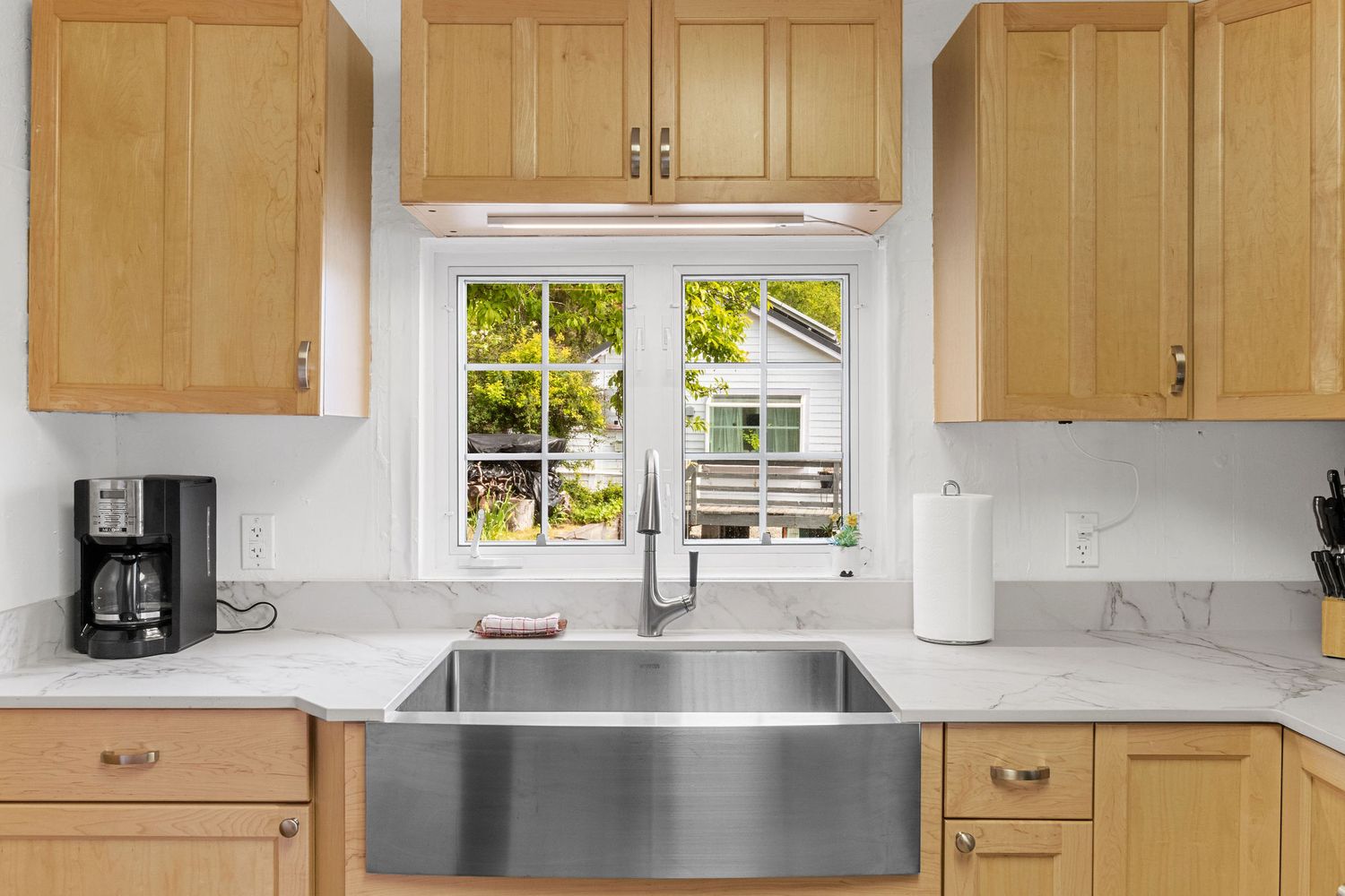 Modern white kitchen with maple cabinets, stainless steel sink, and bright windows overlooking waterfront views.