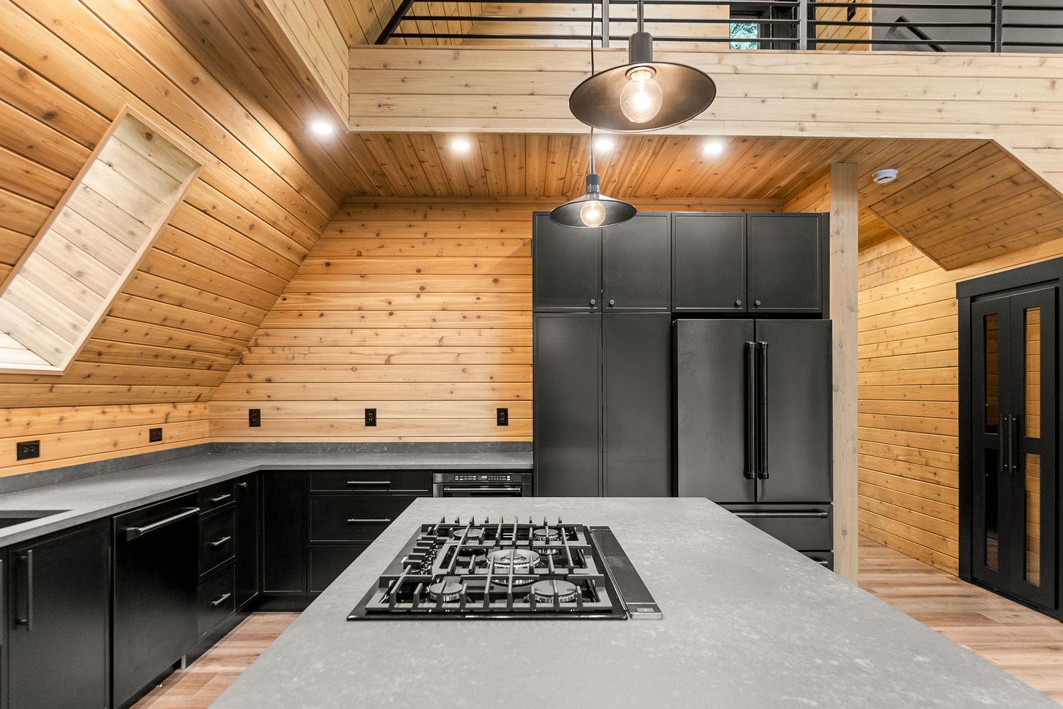 Modern kitchen featuring gas cooktop on grey island with pine wood ceiling and black cabinets.