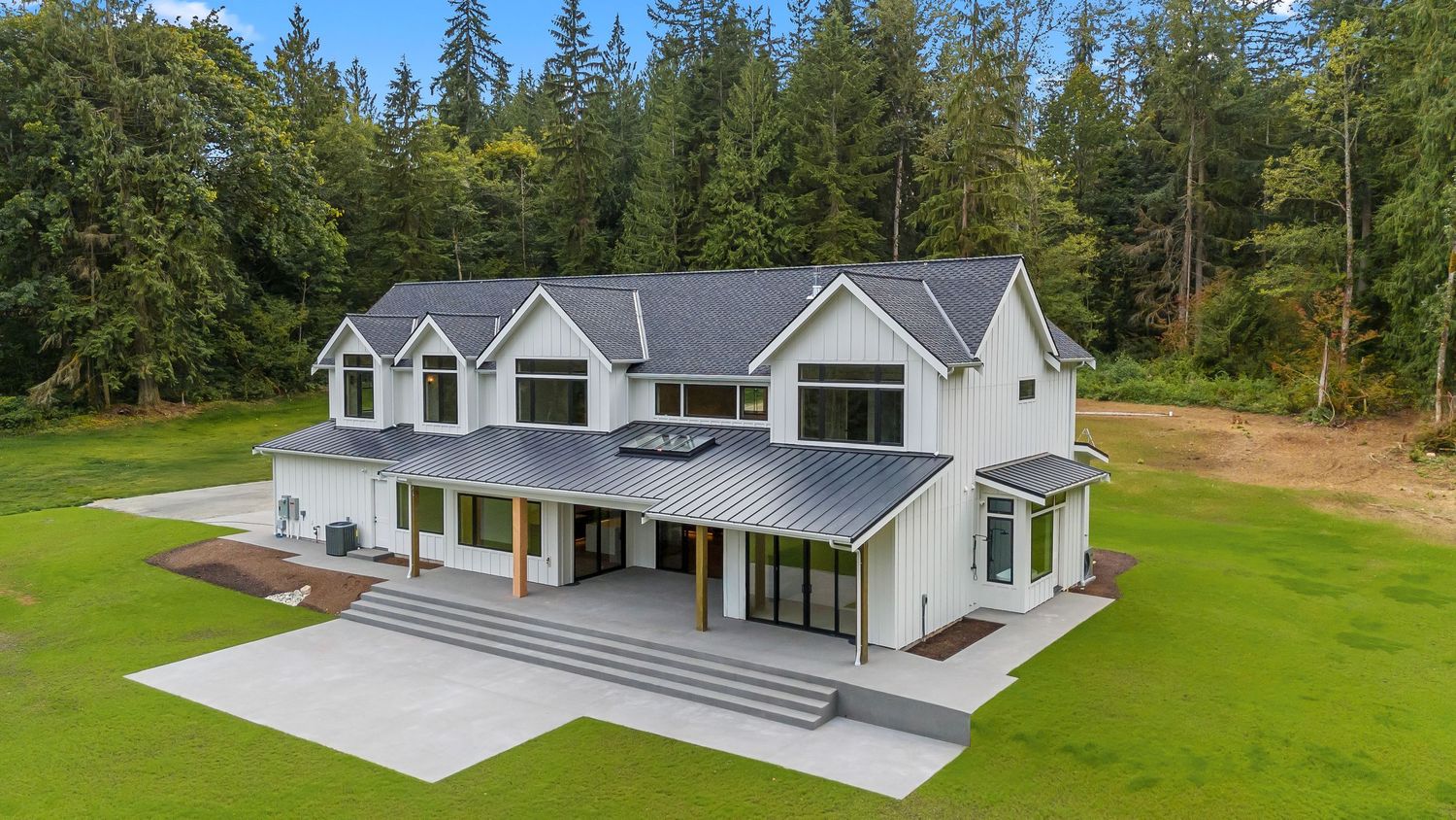 Aerial view of a large contemporary house with grey roof nestled among trees and manicured lawn.