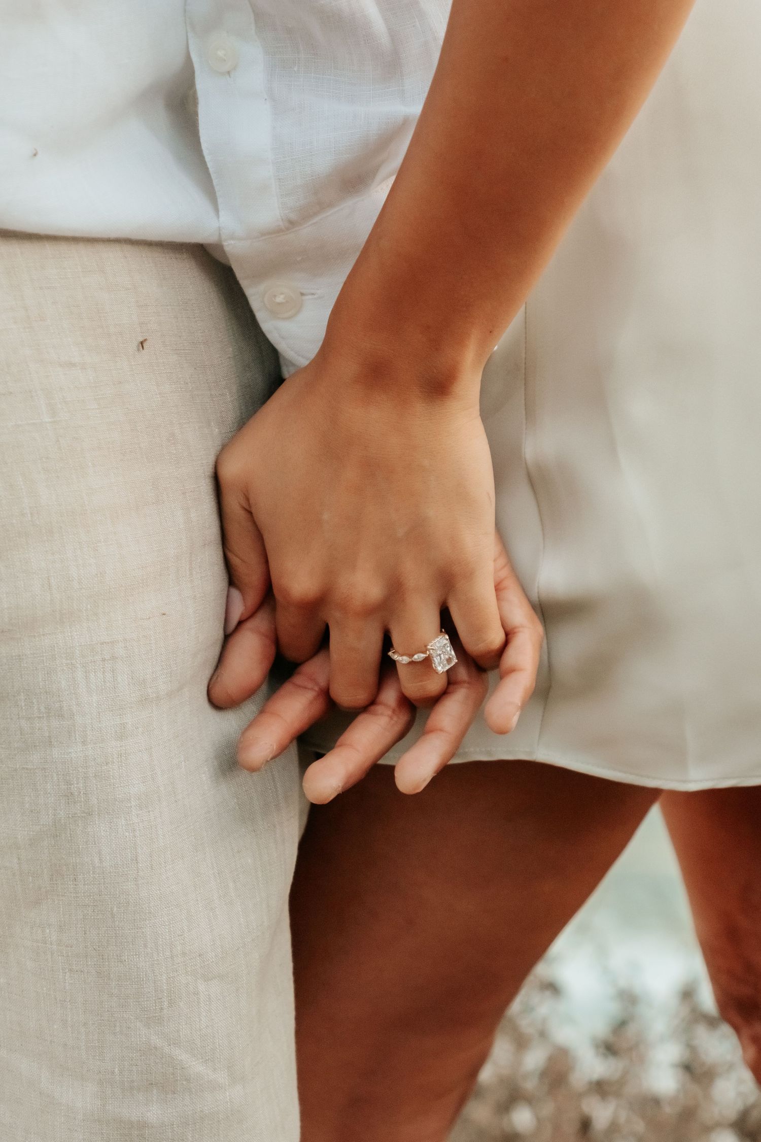 Close-up of couple holding hands showing a sparkling diamond engagement ring outdoors.