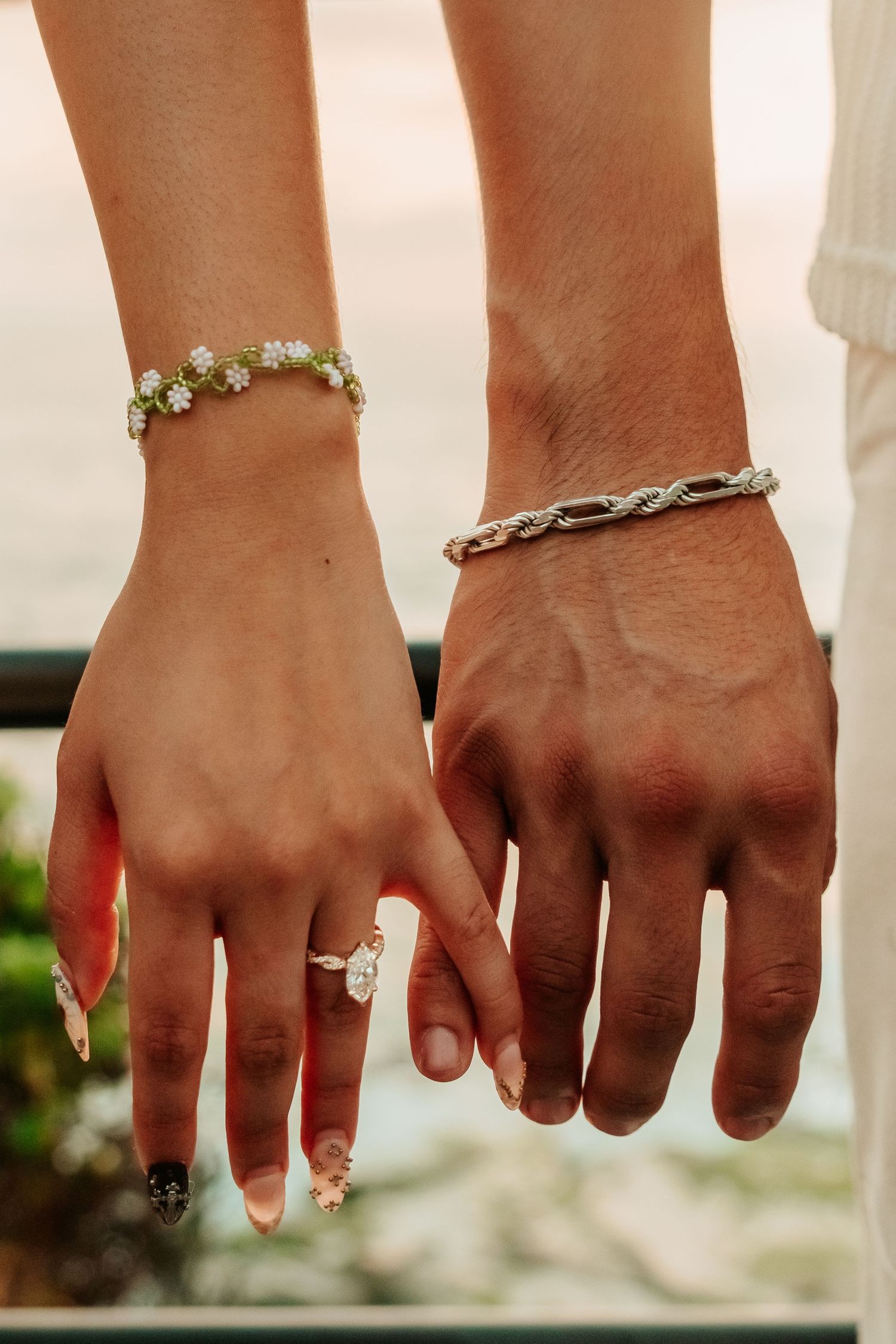 Close-up of engaged couple's hands showing diamond ring and matching bracelets.