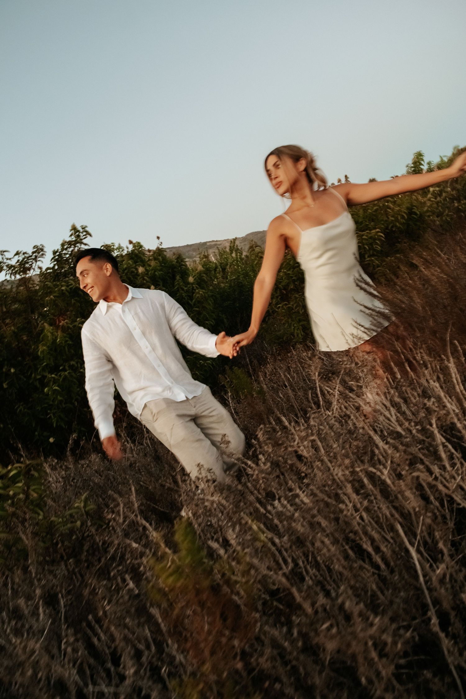 Happy couple holding hands walking through golden field at sunset.