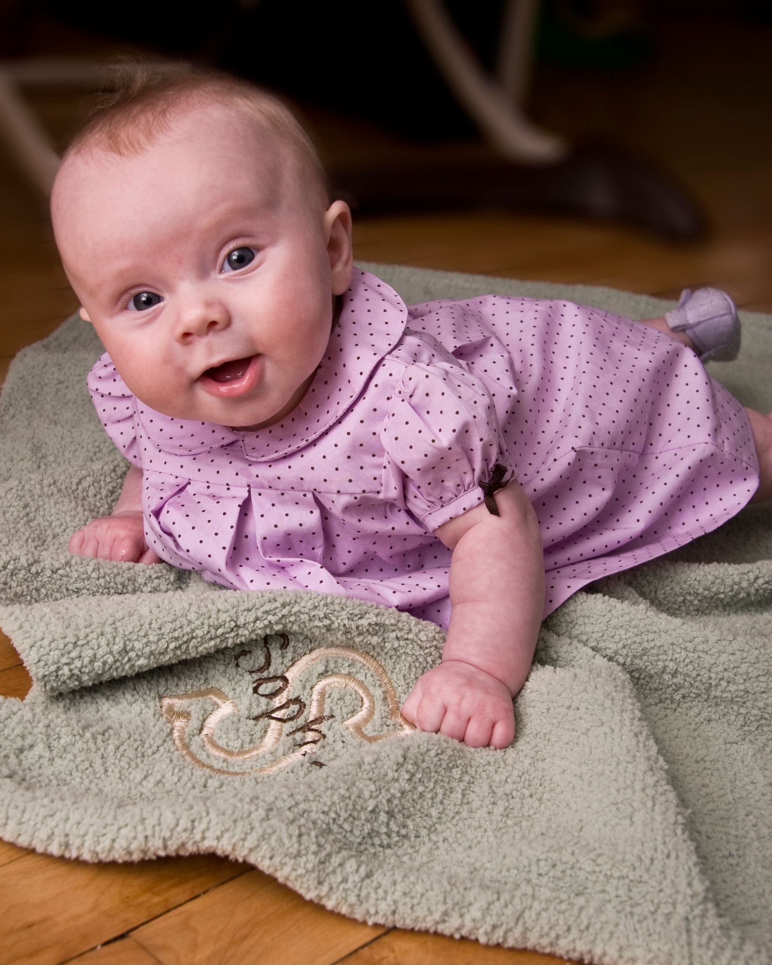 Adorable baby girl in pink polka dot dress does tummy time on a soft green monogrammed blanket.