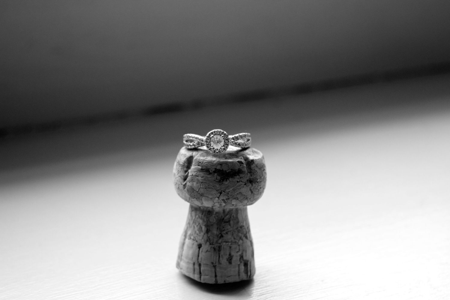 Diamond engagement ring balanced on champagne cork in black and white wedding photo.