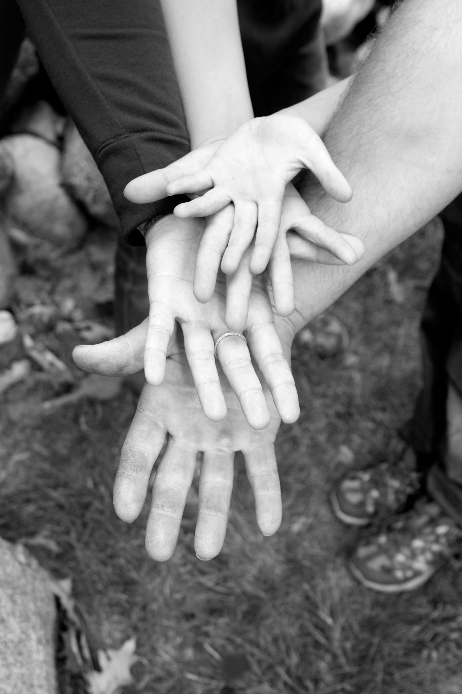 Black and white photo of a family stacking hands together outdoors, symbolizing unity and togetherness.