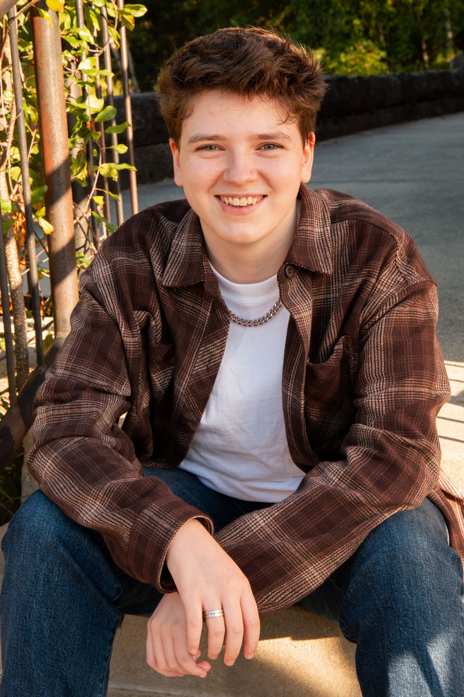 Smiling teenage boy in a brown plaid shirt and jeans sitting on outdoor steps in warm sunlight.