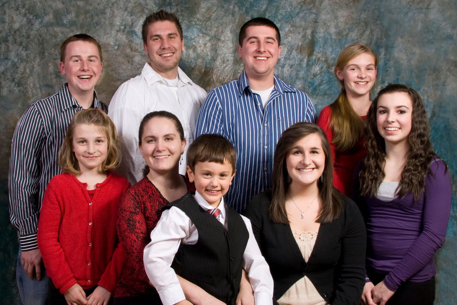 Large family group of nine people poses together smiling in a professional studio portrait photo.