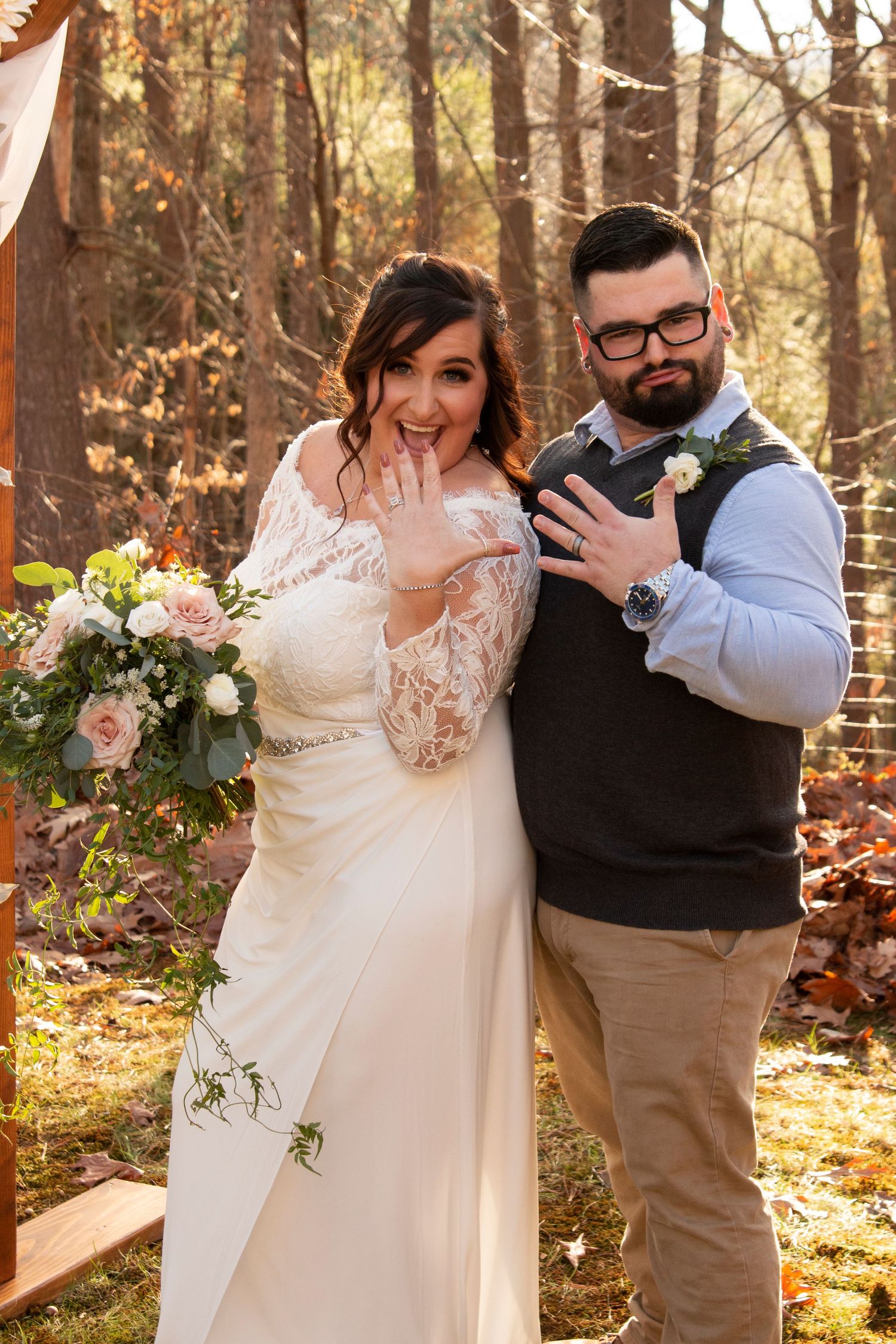 Newlyweds show off wedding rings outdoors in autumn forest wedding setting.