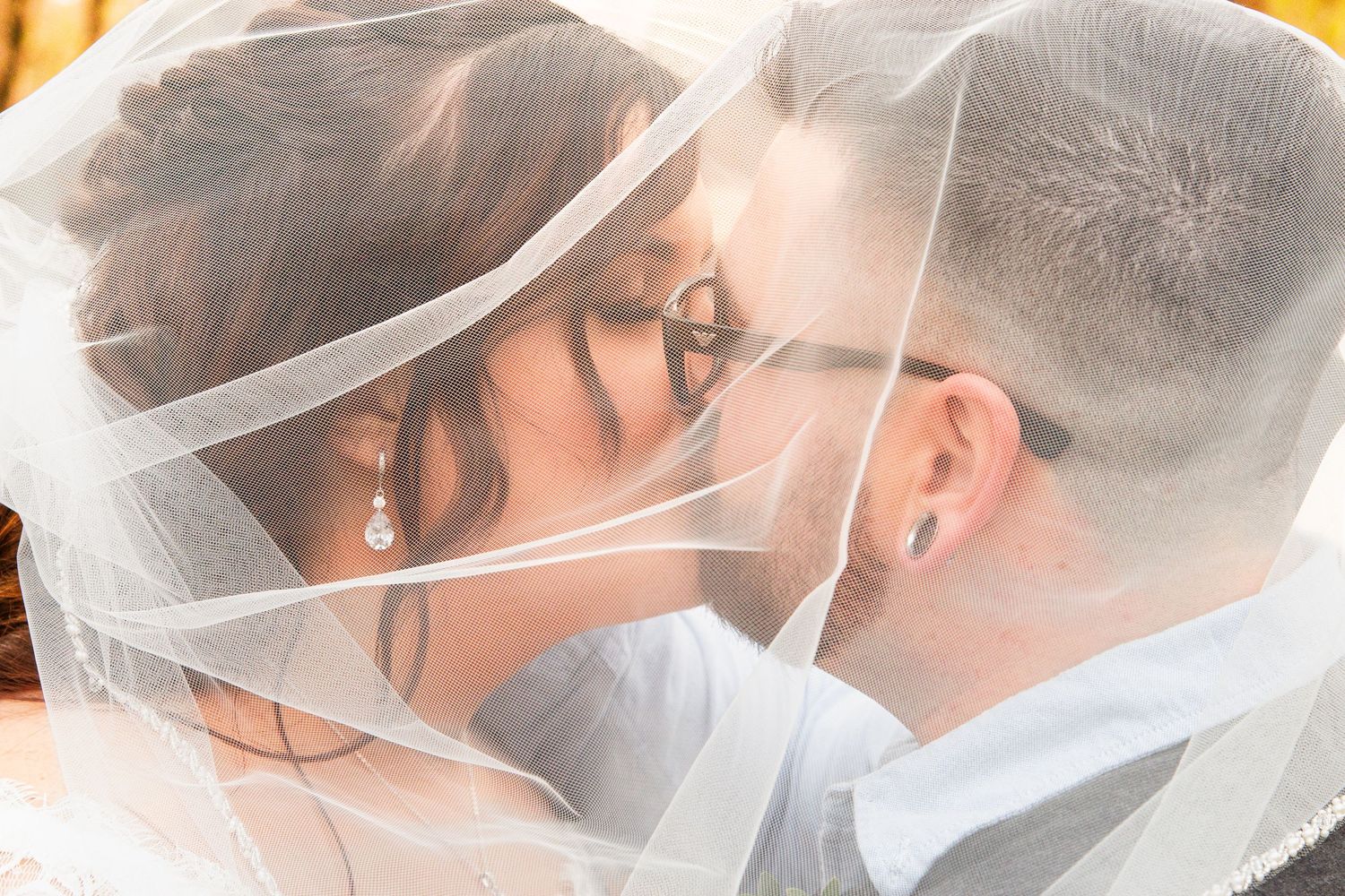 Bride and groom sharing intimate kiss under wedding veil in close-up romantic portrait.