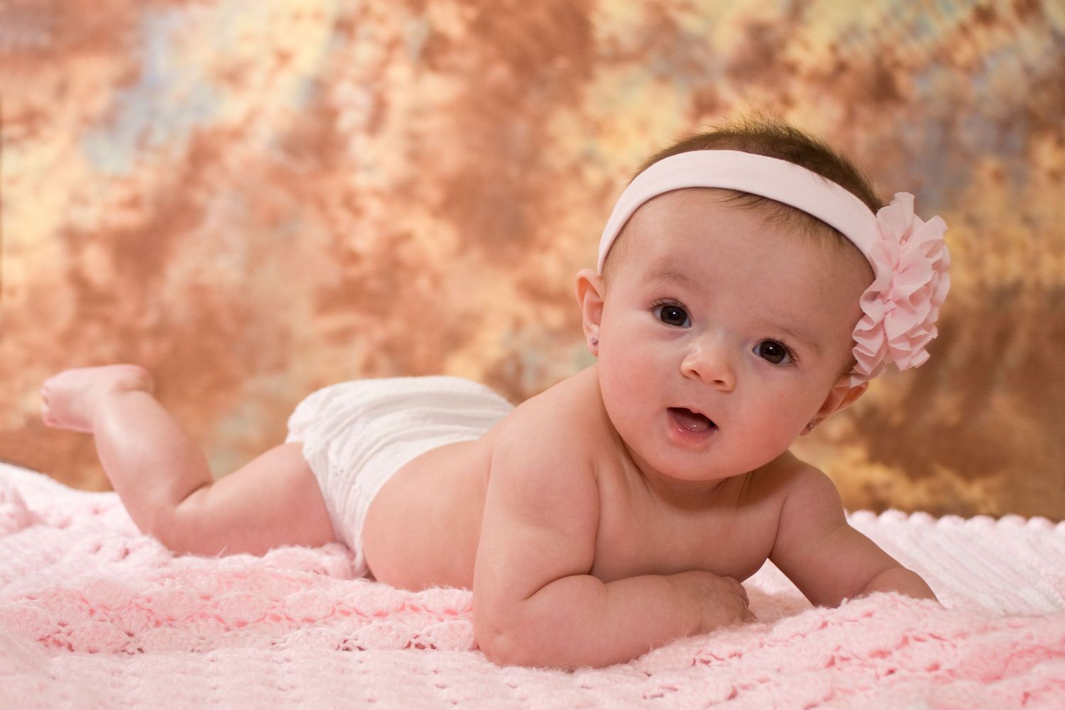 Beautiful baby girl in diaper with pink floral headband lying on pink knit blanket.
