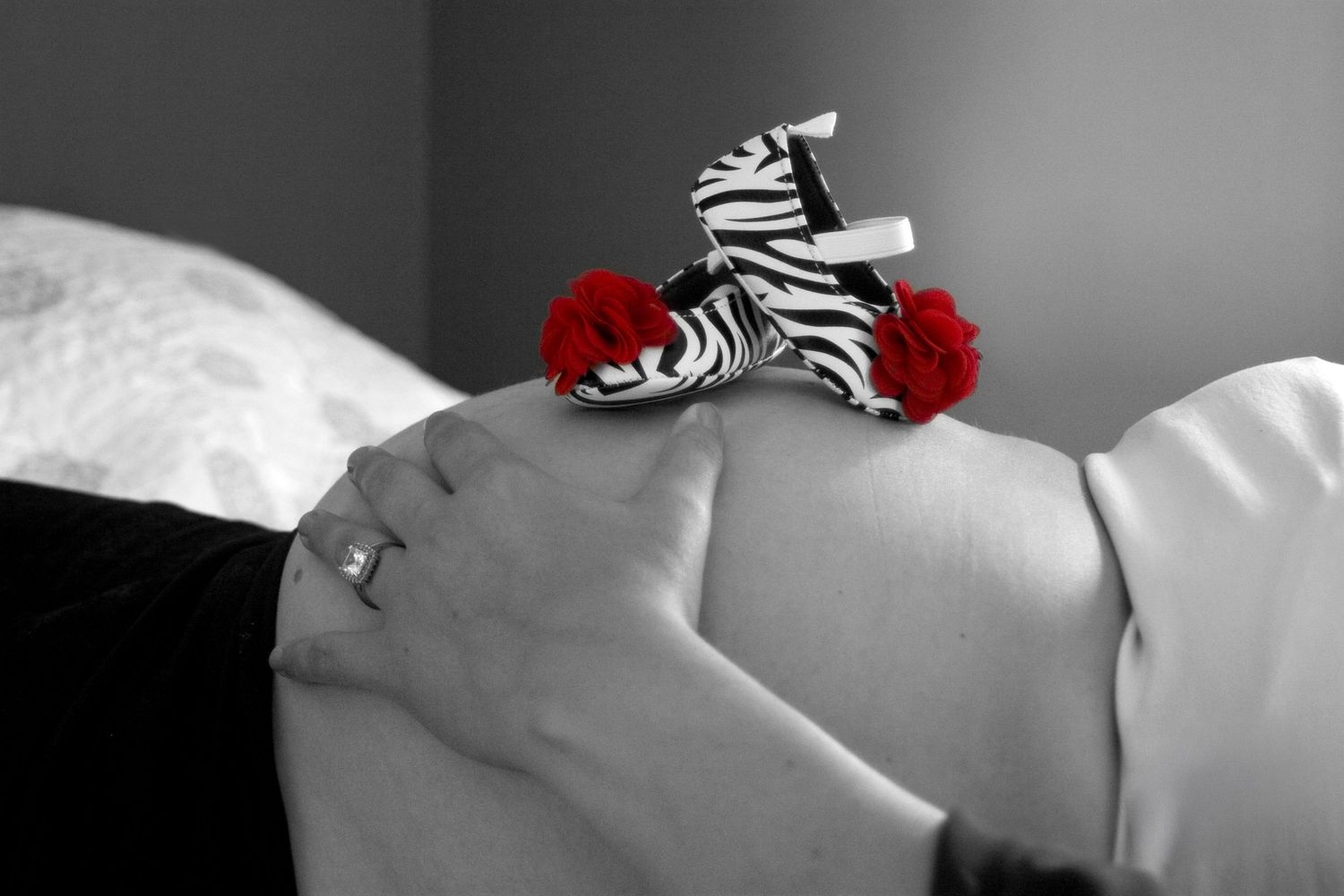 Black and white maternity photo with zebra print baby shoes with red roses on pregnant belly.