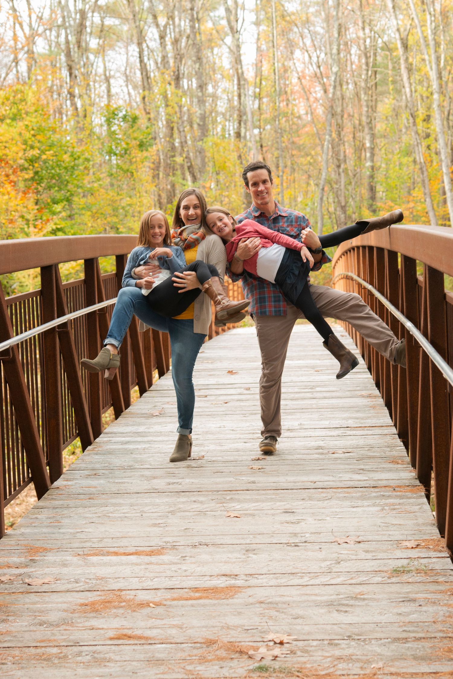 Joyful family of four playfully posing on wooden bridge surrounded by colorful autumn foliage.